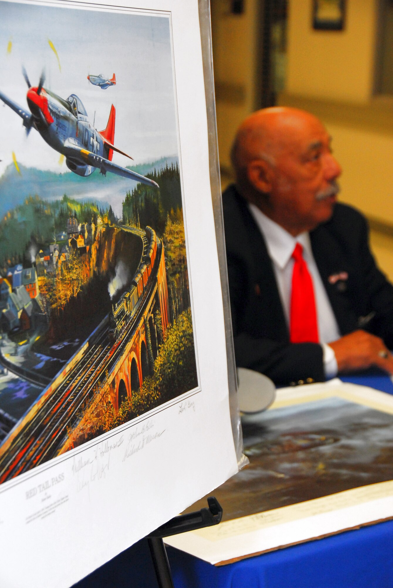 Retired Lt. Col. William Holloman, one of the original Tuskegee Airmen, signs autographs near a lithograph depicting the Tuskegee Airmen in combat during World War II at Maxwell Air Force Base, Ala. (U.S. Air Force photo/Scott Knuteson) 
