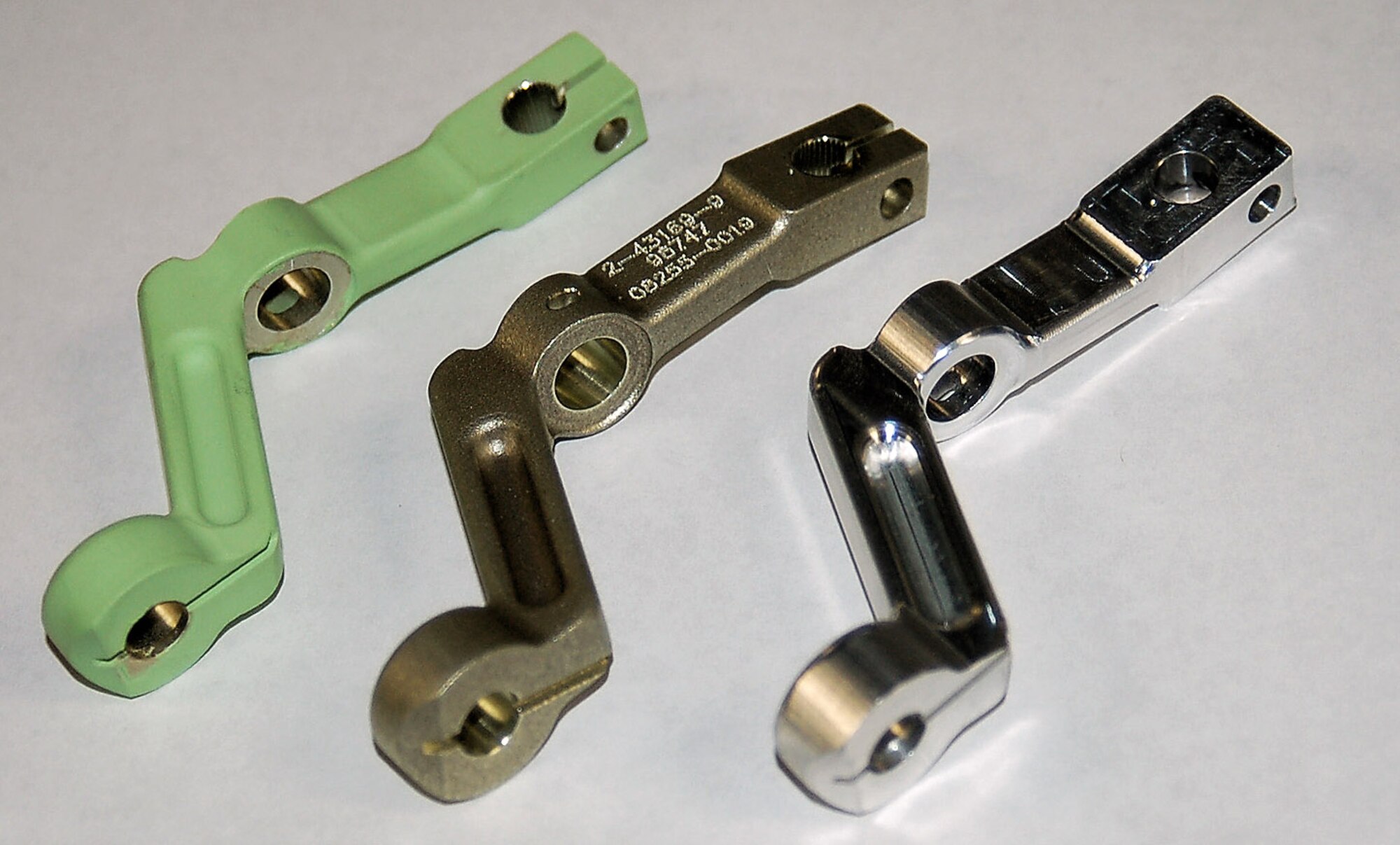 The three steps in the manufacturing process of T-38 aileron levers are shown: first, the part is custom cut (right), then numbered and textured (center), and finally painted green and shipped to the customer. (Air Force photo/Bill Orndorff) 
