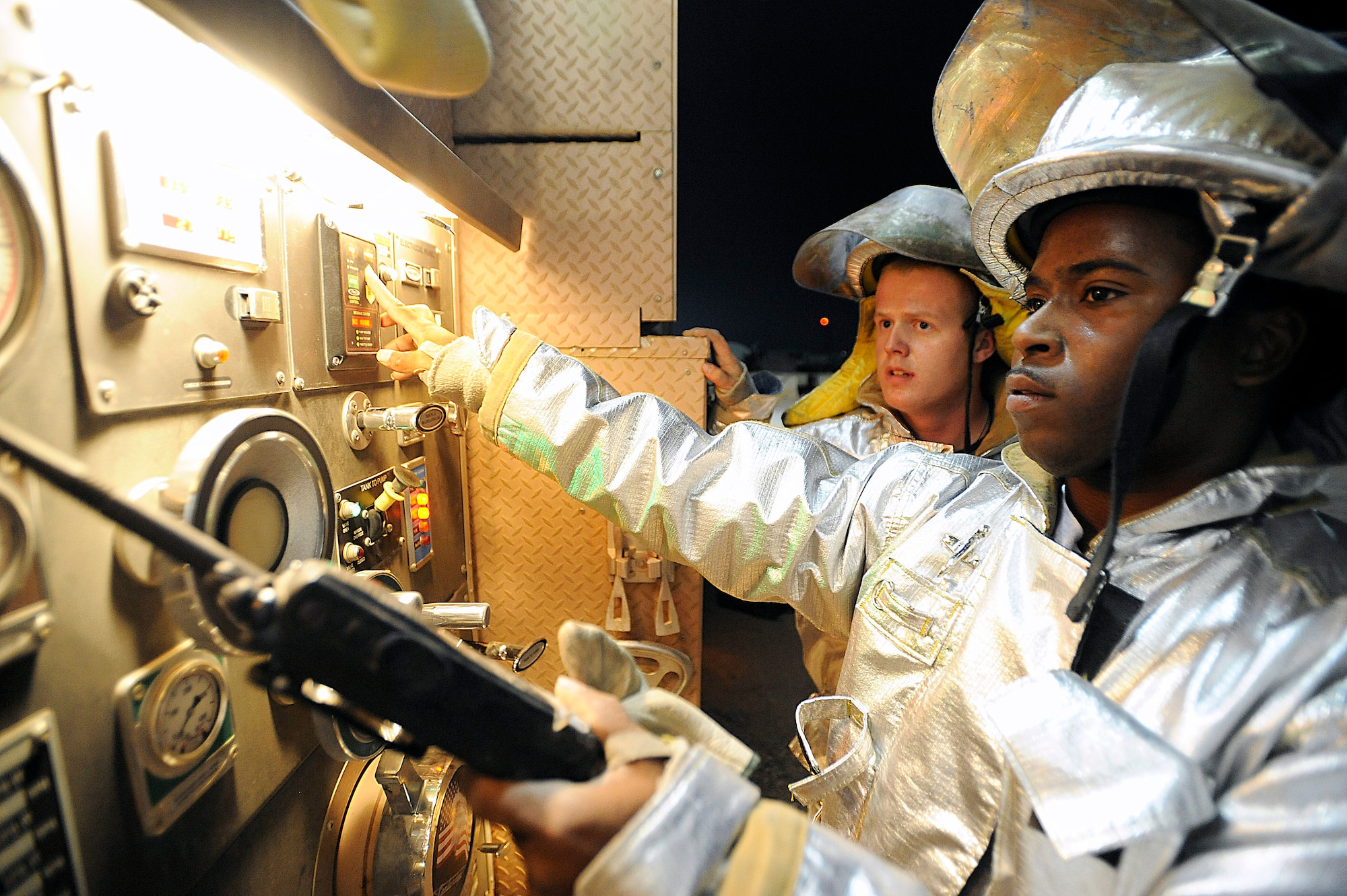 Senior Airman Daniel Utley monitors fire engine controls as Airman 1st Class Jason Kennedy observes during a live-fire training scenario Oct. 22 at Joint Base Balad, Iraq. The Joint Base Balad Fire Department conducted the training to give individual firefighters experience using hose patterns on interior fires. Both Airmen are assigned to the 332nd Expeditionary Civil Engineer Squadron. Airman Utley is deployed from Dyess Air Force Base, Texas, and Airman Kennedy is deployed from Dover AFB, Del. (U.S. Air Force photo/Airman 1st Class Jason Epley) 
