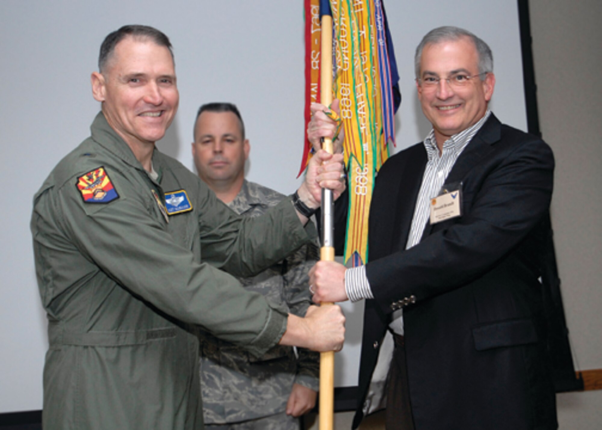 Brig. Gen. Kurt Neubauer, 56th Fighter Wing commander, and Don Brandt, Arizona Public Service CEO and the wing's new honorary commander, hold the 56th FW guidon Saturday during the new honorary commanders induction ceremony. Chief Master Sgt. Randy Raper, 56th FW command chief, looks on. (U.S. Air Force photo/ Master Sgt. William Gomez.)