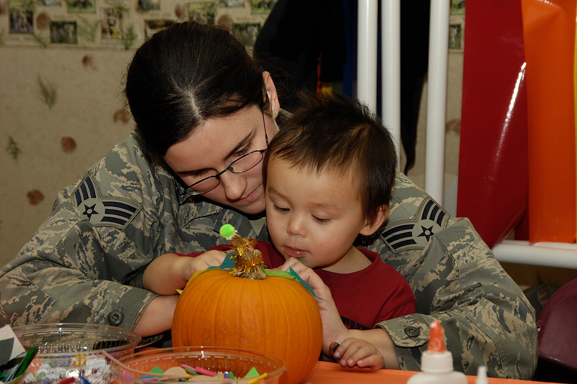 HANSCOM AIR FORCE BASE, Mass. – Pumpkins, glitter glue, cider and donuts all played a part in bringing smiles to the faces of Child Development Center families on Oct. 28, during a parent and child pumpkin decorating event held at the CDC. Pictured here Senior Airman Melissa Nguyen helps her son Aden put the finishing touches on his pumpkin during the activity. (U.S. Air Force photo by Linda LaBonte Britt)

