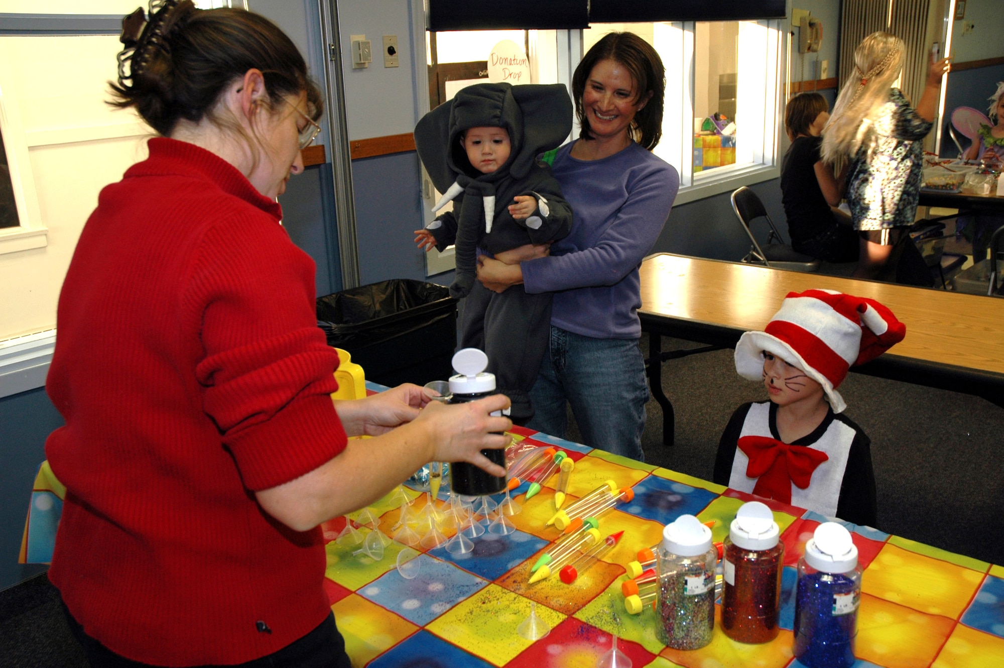 Linda Bivens, event volunteer, pours glitter into a glitter pen for Amy Reno, Dominic, 2, and Cristian, 5, during the Harvest Festival Oct. 27 at the base chapel annex. Children also had the opportunity to make tambourines, snow globes, Thanksgiving wreaths, bracelets, and play games to win prizes. (U.S. Air Force photo/Airman 1st Class Dillon White) 