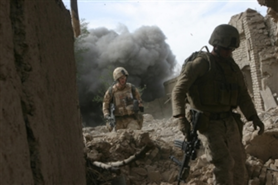 U.S. Marine Corps Cpl. Kyle Page (right), a team leader with 3rd Combat Engineer Battalion, attached to Fox Company, 2nd Battalion, 7th Marine Regiment, and an Estonian Defense Forces service member make their way over rubble in Northern Now Zad, Afghanistan,  as a controlled detonation explodes behind them on Oct. 26, 2008.  Marines are conducting a clearing operation of a known enemy stronghold in support of an Estonian Defense Force vehicle checkpoint.  