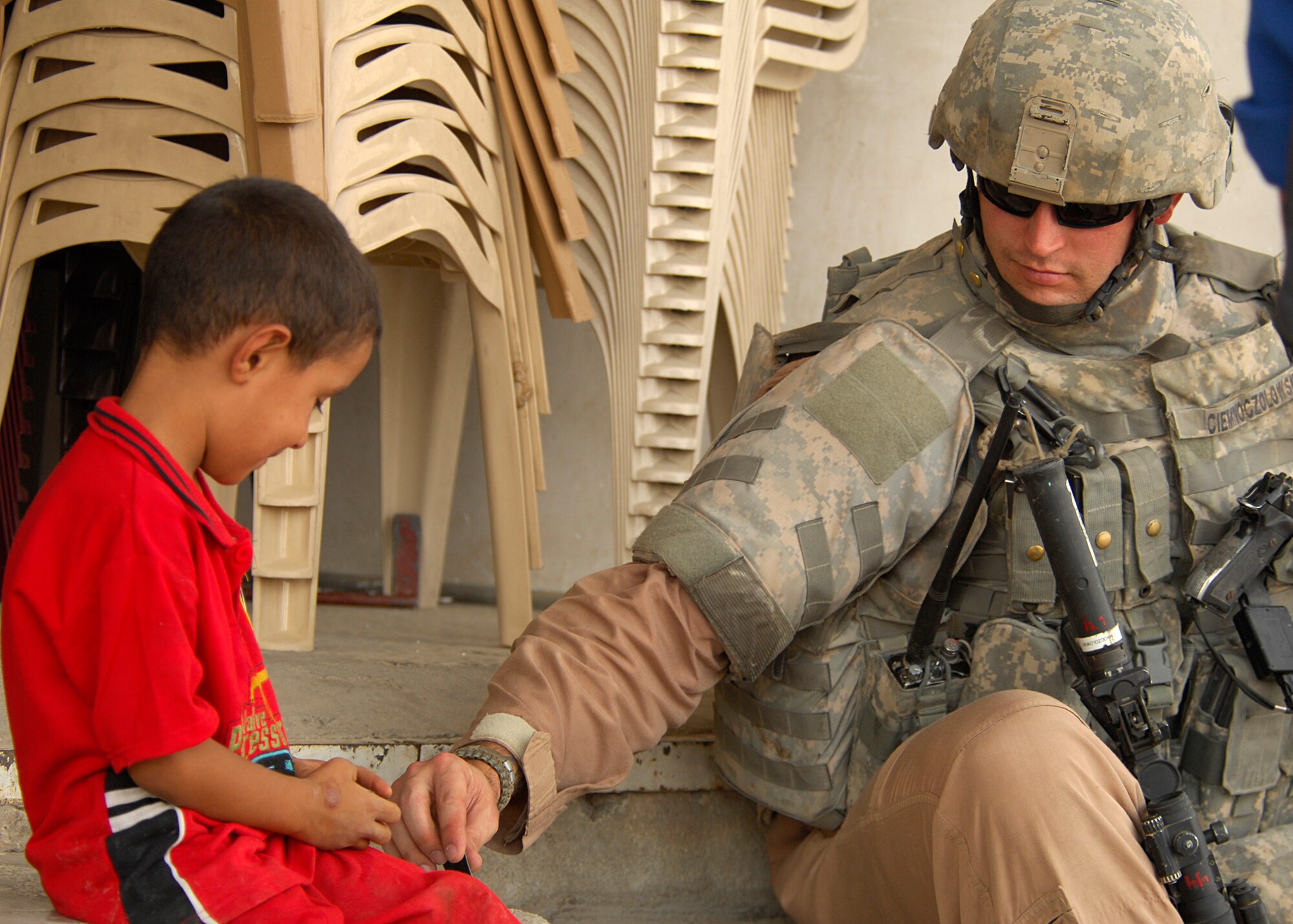 DOURA, IRAQ -- Staff Sgt. Isaac Ciemnoczolowski builds a matchbook house with an Iraqi boy during a combined patrol with Iraqi police Aug. 30. The patrol was training for Iraqi police in tactics, techniques and procedures here. Ciemnoczolowski is one of more than 150 Joint Source Solution Airmen assigned to the 732nd Expeditionary Security Forces Squadron, Det. 3, which performs Police Transition Team missions at six Iraqi police stations and one Iraqi police district headquarters in the East and West Rasheed Districts of Baghdad. The 732nd ESFS, Det. 3, stationed at Victory Base in Baghdad, also supports two 24-hour Joint Security Stations. JSS Airmen are assigned duties outside their normal Air Force specialties to fill in vacant positions that Soldiers cannot support due to the Army's heavy theater operations tempo. Ciemnoczolowski is deployed from Minot Air Force Base, N.D. (U.S. Navy photo/Petty Officer 2nd Class Kelvin Surgener)  