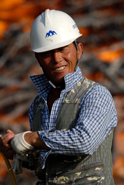 Mr. Je Ho So, a laborer working for Ausko Construction, glances back while spraying down the ground around a burning pile of trees that have been infected with Pine Blight to keep the fire from spreading on 30 Aug 2008 at Kunsan AB, South Korea.  The trees were burnt to keep the other trees in the area from being infected with the disease. (U.S. Air Force photo/Staff Sgt. Jason Colbert)