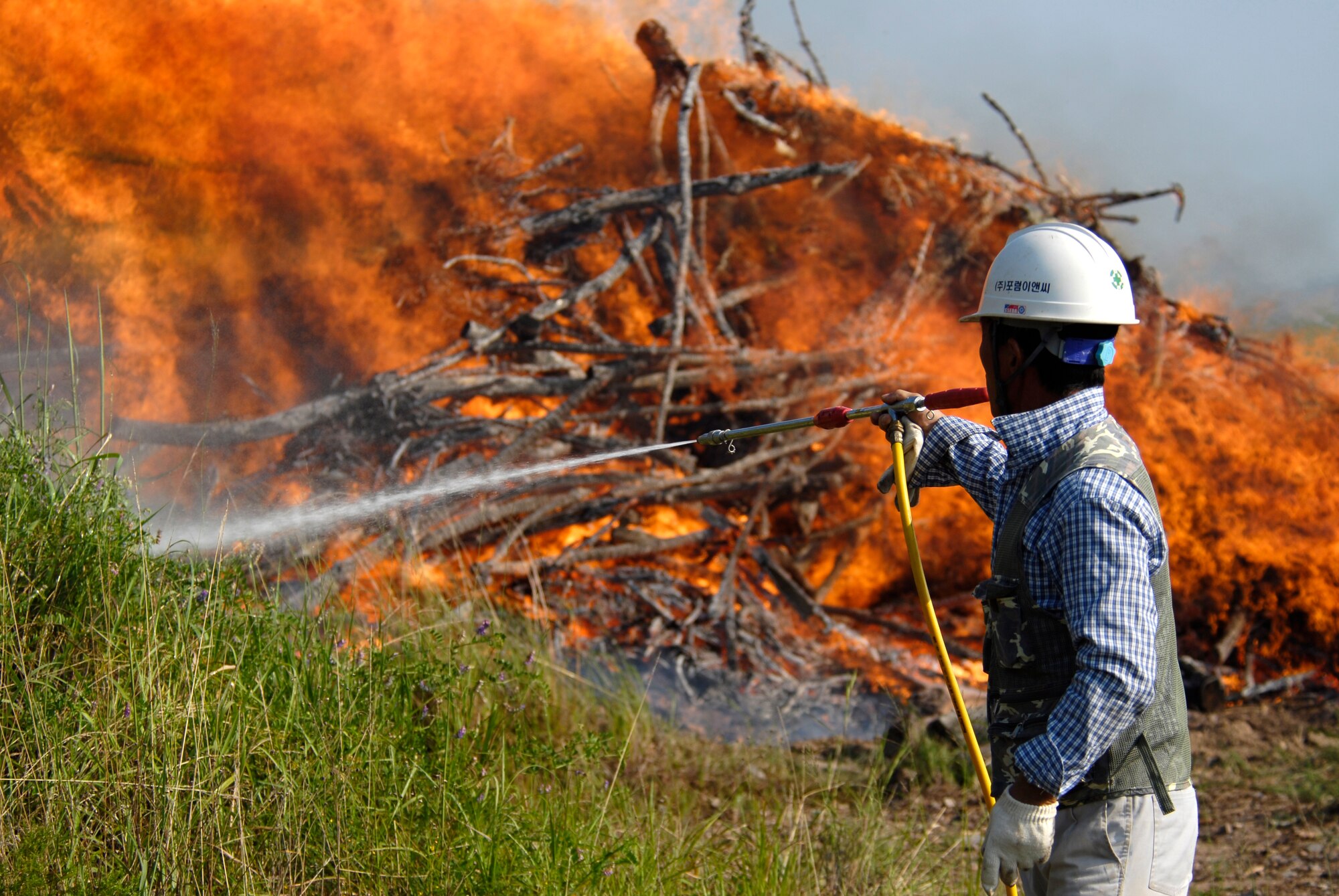 Local contractor, Je Ho So, wets the ground around a burning pile of tree limbs with Pine Blight to keep the fire from spreading here Aug. 30. The limbs were removed and burned to eradicate the infection and prevent it from spreading to other trees in the area. (U.S. Air Force photo/Staff Sgt. Jason Colbert)