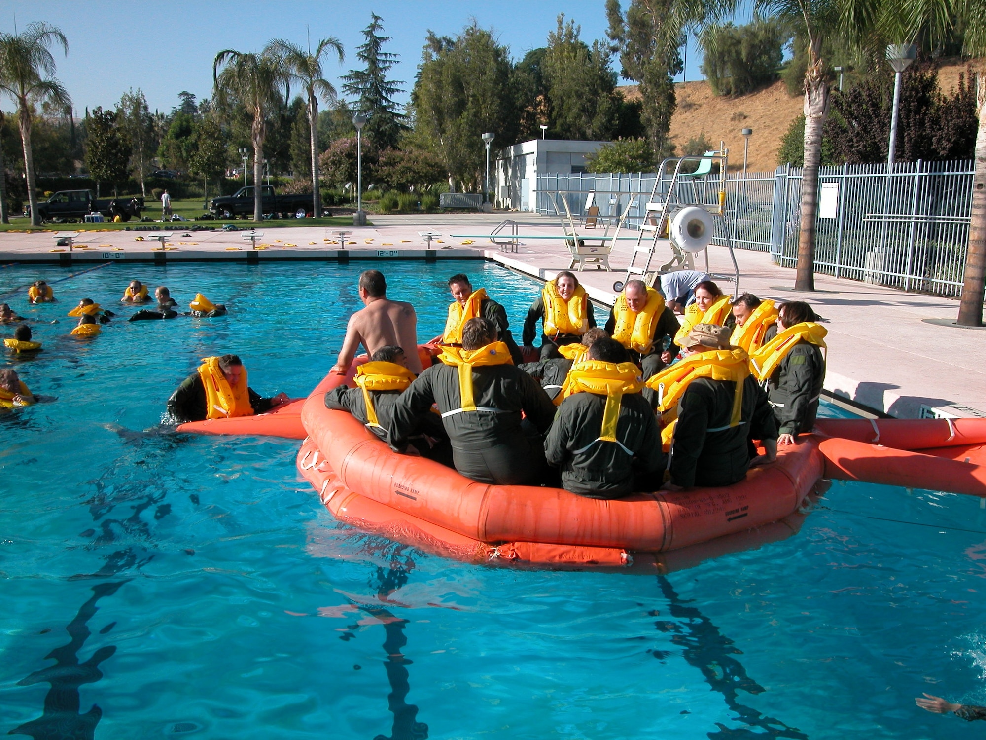 Tech. Sgt. Lawrence Hill, lead instructor (in raft, no shirt), shows an Airman how to properly climb up the boarding ramp of a 20-man life raft during a combat and water survival course at Loma Linda University’s Dryson Sports Center. (U.S. Air Force photo by Staff Sgt. Joe Davidson, 452 AMW/PA)