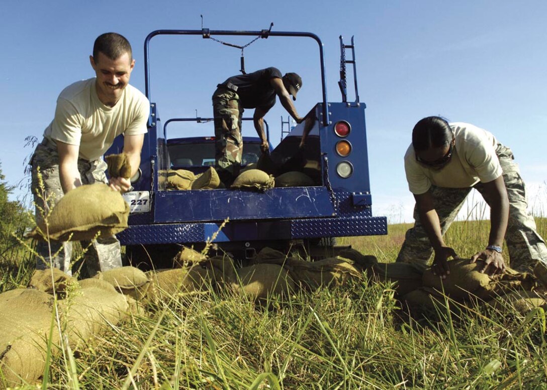 Airman First Class Daniel Dowell, Airman Daniel Morrow and Staff Sgt. Lesette Fraser, 744th Communications Squadron members, unload a truck of sandbags to build defensive fighting position barriers at the security forces training ground Sept. 3. The 844th Communications Group held a warrior day event Sept. 4 testing skills that would be used on deployment such as self aid buddy care, throwing gernades, low crawl and detecting unexploded ordnances. (U.S. Air Force photo by Senior Airman Renea Kleckner)
