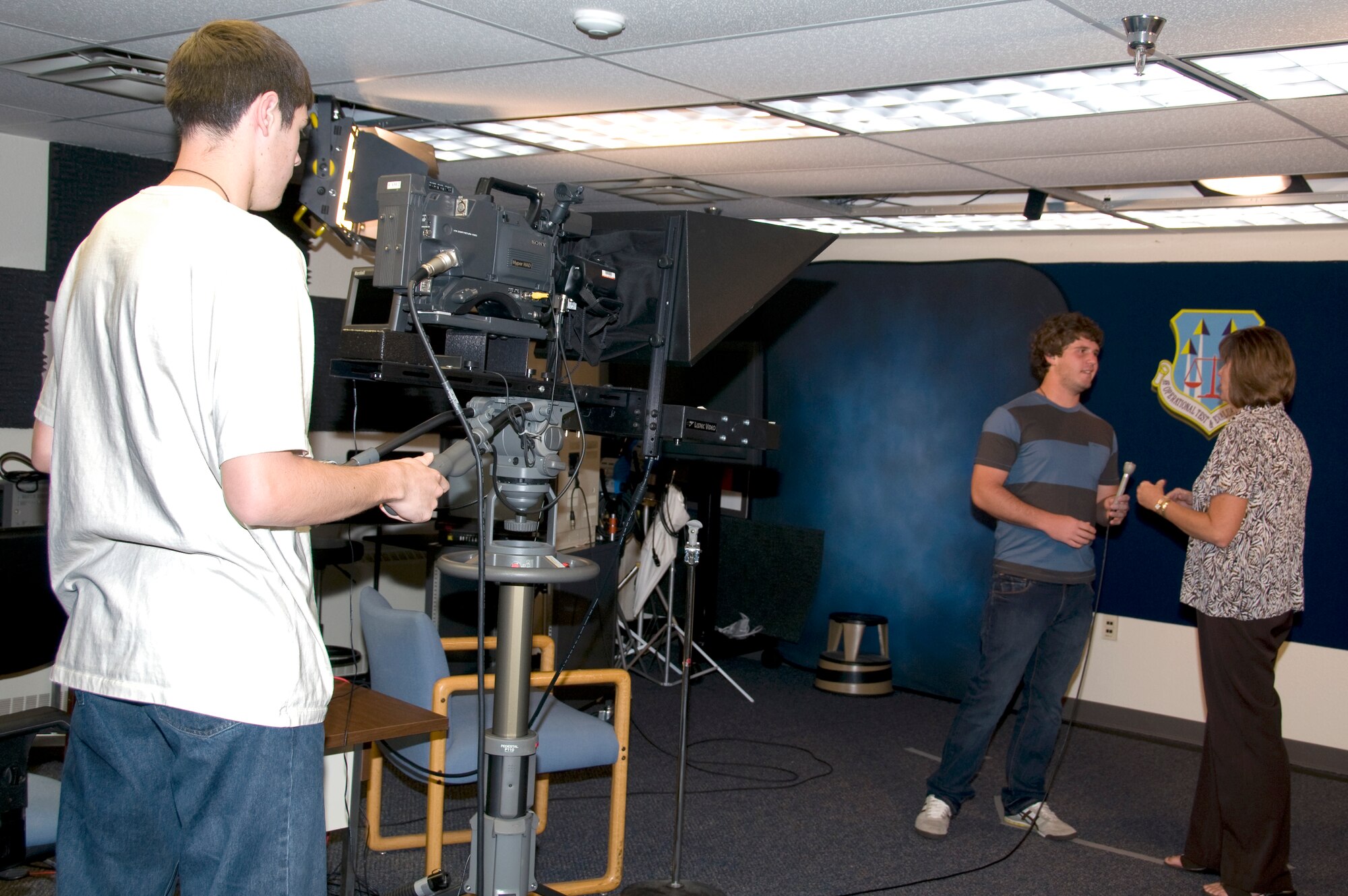 Ethan Halliday, left, a student intern with the Air Force Operational Test and Evaluation Center Multimedia Division, operates the camera as Calum Murray, a student intern with AFOTEC Public Affairs, practices his on-camera interviewing skills with Katherine Gandara, AFOTEC  Chief of Public Affairs. 