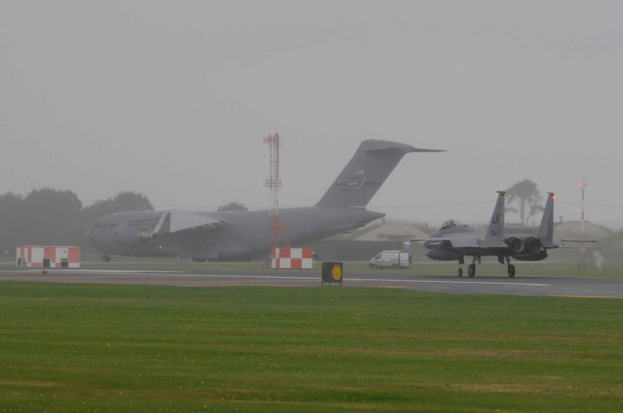 A C-17 waits on the taxi-way for an F-15 Eagle to exit the runway so it can fly back to McChord AFB, Wash. after stopping overnight for rest and fuel at RAF Lakenheath, England, Sept. 4. The runway at RAF Lakenheath allows for C-17's and larger aircraft to land and transport Airmen and cargo in support of AEF. (U.S. Air Force photo by Senior Airman Brian J. Ellis)