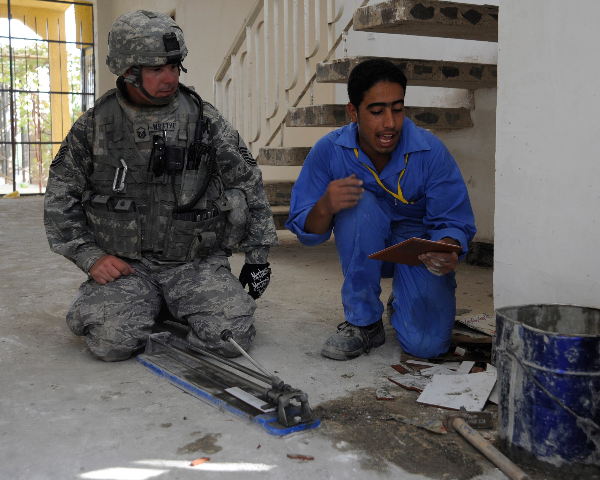 HAWR RAJAB, IRAQ -- U.S. Air Force Master Sgt. Patrick Wrathell, 1st Sgt. non-commissioned officer in charge of downtown operations with 557th Expeditionary RED HORSE squadron, shows an Iraqi student worker how to cut tile at Hawr Rajab, Iraq on Aug. 27. Wrathell, a East Tawas, Mich. native, is deployed from 823rd RED HORSE squadron, Hurlburt Field, Fla. (U.S. Air Force photo/Staff Sgt. Paul Villanueva II)