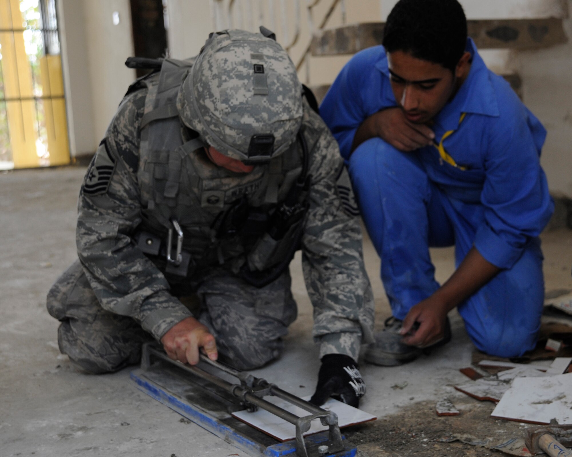HAWR RAJAB, IRAQ -- U.S. Air Force Master Sgt. Patrick Wrathell, 1st Sgt. and non-commissioned officer in charge of downtown operations with 557th Expeditionary RED HORSE squadron, shows an Iraqi student worker how to cut tile at Hawr Rajab, Iraq on Aug. 27. Wrathell, a East Tawas, Mich. native, is deployed from 823rd RED HORSE squadron, Hurlburt Field, Fla. (U.S. Air Force photo/Staff Sgt. Paul Villanueva II)