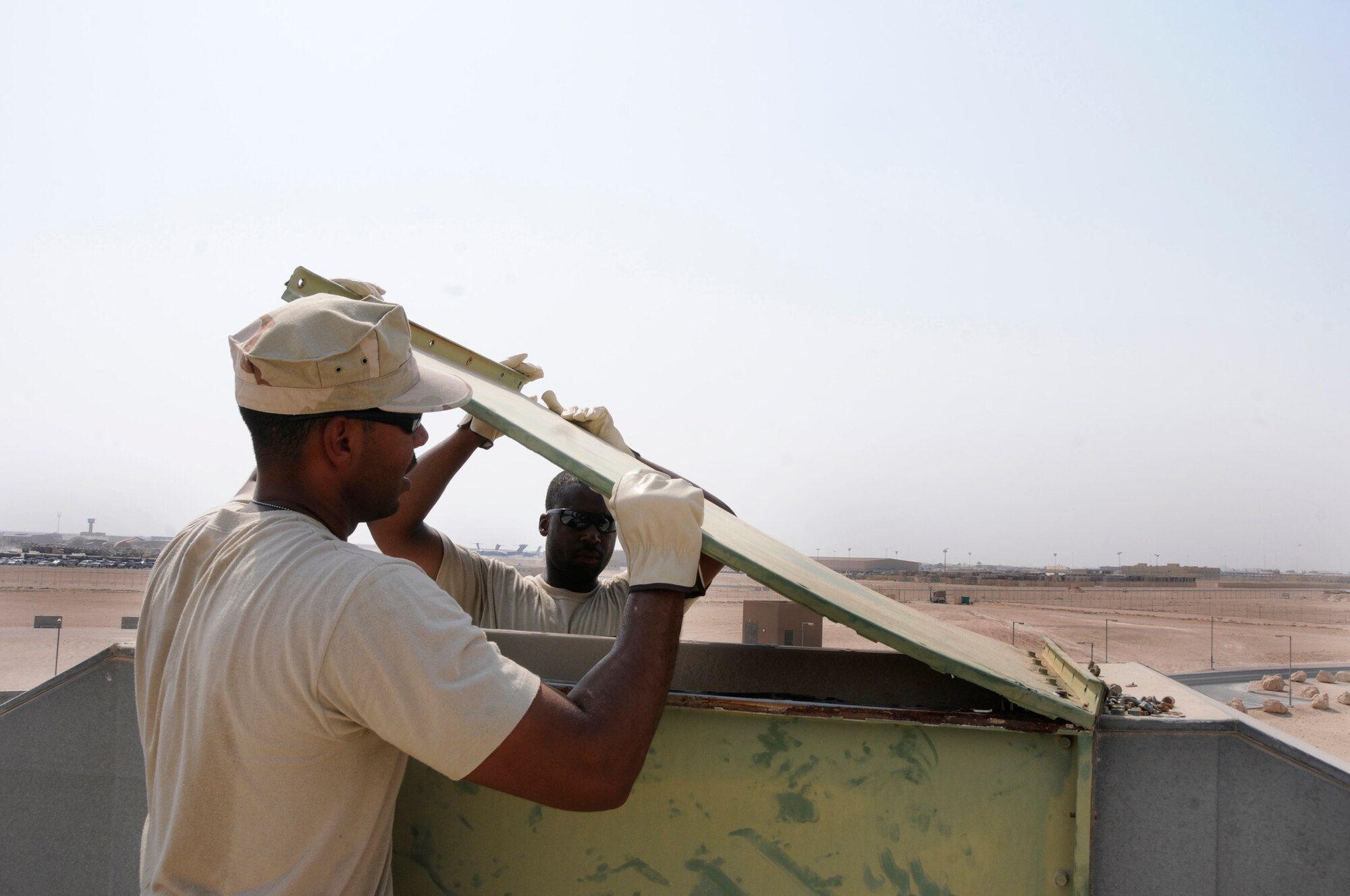 Staff Sgt. Darren Cook and Senior Airman Stephen James, 379th Expeditionary Civil Engineer Squadron, removes a fresh air intake cover Sept. 6, 2008.  The cover is being removed to facilitate a routine cleaning of the intake system on the roof of living quarters at this undisclosed air base in Southwest Asia.  Sergeant Cook is a native of Decatur, Ga., and Airman James is from Miami, Fla. Both are deployed here from Andrews Air force Base, Md., supporting Operations Iraqi and Enduring Freedom and Joint Task Force-Horn of Africa.  (U.S. Air Force photo by Tech. Sgt. Michael Boquette/Released)
