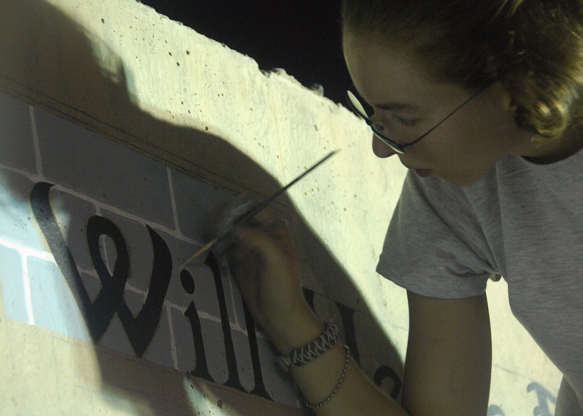 SOUTHWEST ASIA -- Senior Airman Beth Weaver-Henderson, assigned to the 386th Expeditionary Security Forces Squadron, touches up the text on a mural she painted Sept. 3 at an air base in Southwest Asia. The three different murals are dedicated to those who were lost on the tragic events of Sept. 11., and represent heroic images from that fateful day. Airman Weaver-Henderson has spent more than three weeks of her off-duty time to complete the murals ahead of schedule for the Sept. 11 commemoration event being held here. Airman Weaver-Henderson is deployed from Travis Air Force Base, Calif. (U.S. Air Force photo/Tech. Sgt. Raheem Moore)