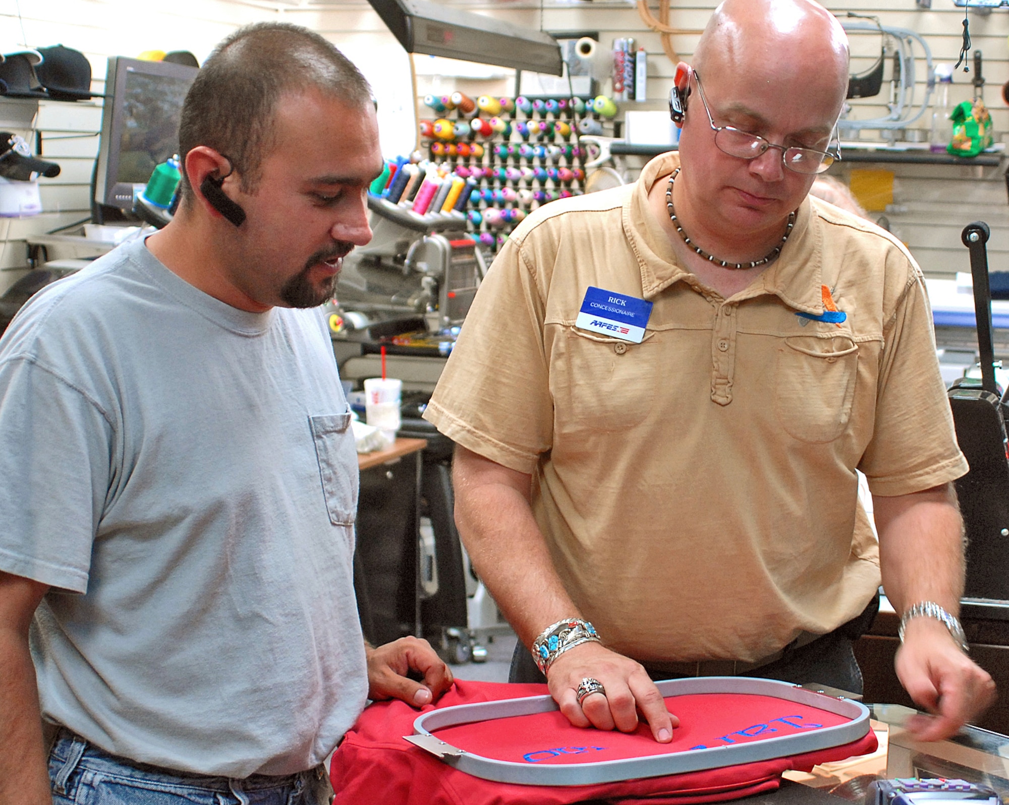 Rick Shankles, right, owner of The T-Shirt Shop, located in the BX consessions area, verifies the correct spelling on customer Jeremy Jaramillo?s shirt. U.S. Air Force photo by Dennis Carlson