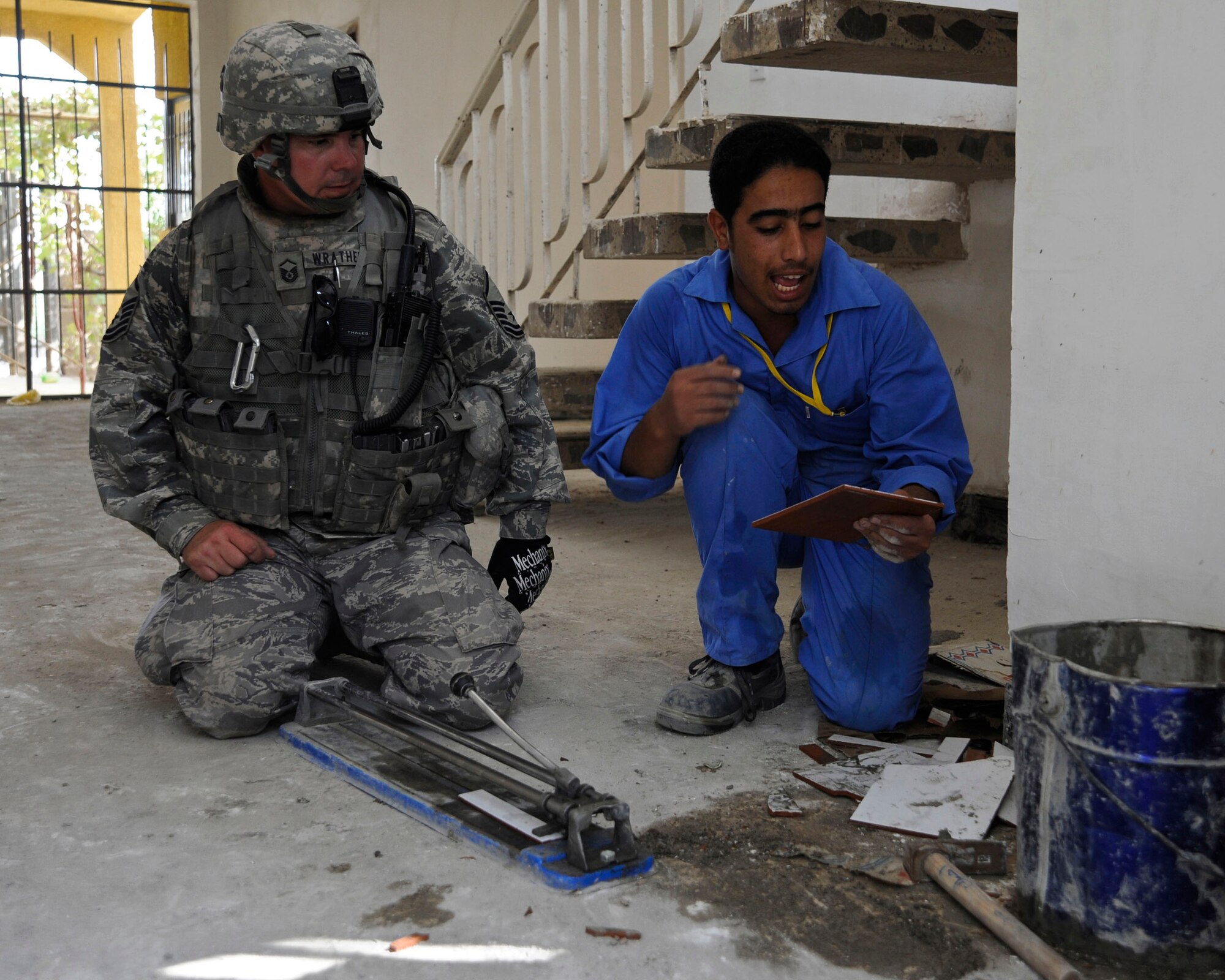 Master Sgt. Patrick Wrathell shows an Iraqi student worker how to cut tile at Hawr Rajab, Iraq, Aug. 27. Sergeant Wrathell is the first sergeant and the NCO in charge of downtown operations for 557th Expeditionary RED HORSE Squadron. (U.S. Air Force photo/Staff Sgt. Paul Villanueva II)