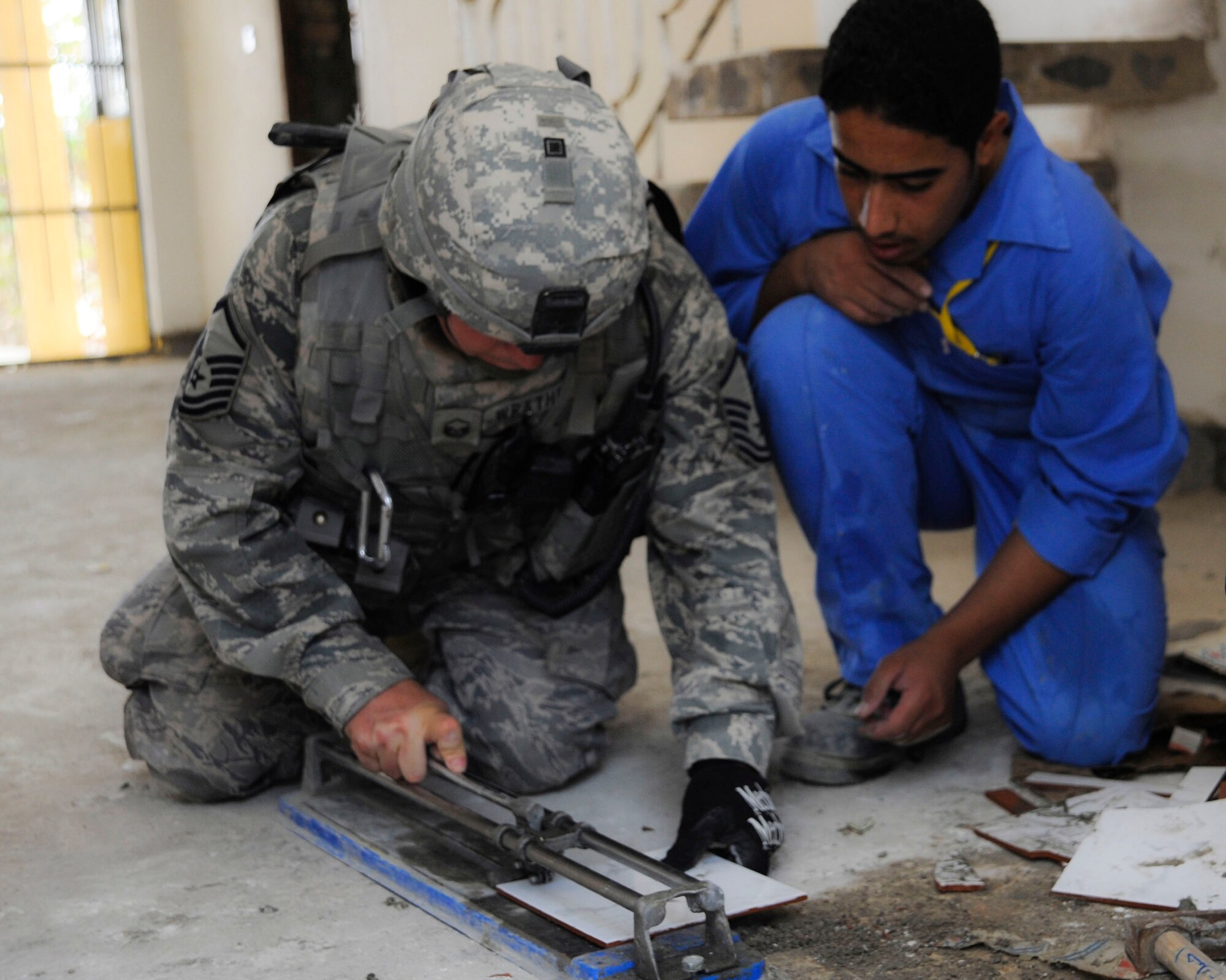 Master Sgt. Patrick Wrathell shows an Iraqi student worker how to cut tile at Hawr Rajab, Iraq, Aug. 27. Sergeant Wrathell is the first sergeant and the NCO in charge of downtown operations for 557th Expeditionary RED HORSE Squadron. (U.S. Air Force photo/Staff Sgt. Paul Villanueva II)