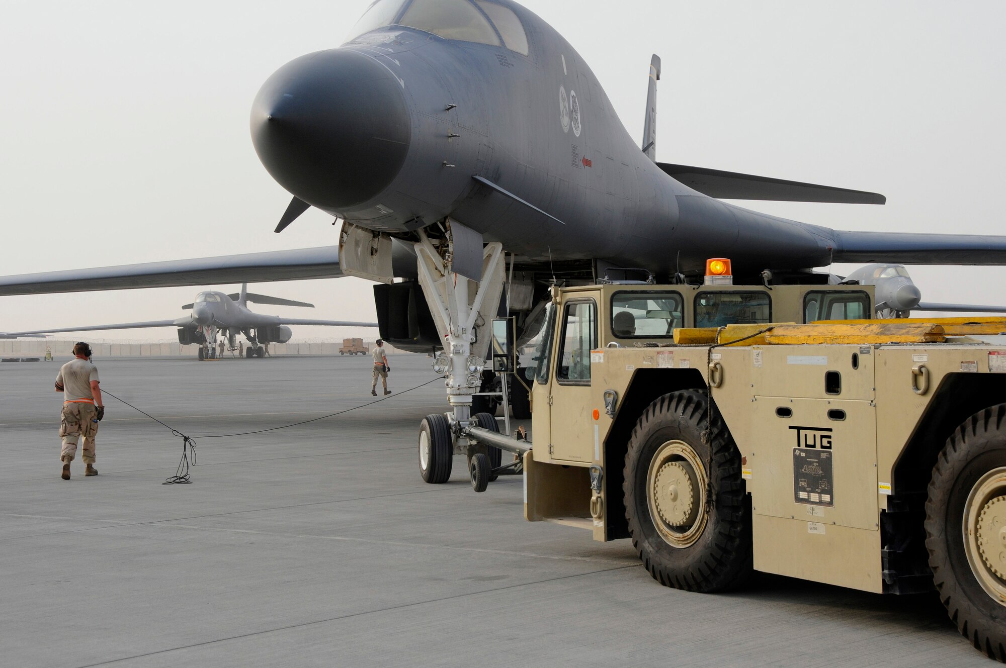 Staff Sergeant Jon Mirro operates a tow vehicle, pushing a B-1 Lancer back into a parking position on the North Ramp here at this undisclosed air base in Southwest Asia Sept. 9, 2008.  Staff Sergeant Scott Shipman, walking beside the B-1, stays in communication with aircrew members in the cockpit who are responsible for working the brakes of the aircraft.  The B-1 is called upon daily to support ground forces engaged in both Operations Iraqi and Enduring Freedom.  It carries the largest payload of both guided and unguided weapons in the Air Force inventory and is the backbone of America's long-range bomber force. It can rapidly deliver massive quantities of precision and non-precision weapons against any adversary, anywhere in the world, at any time. Sergeant Mirro is a native of Ellensburg, Wash., and Airman Decker hails from Murphy, N.C. Both are assigned to the 379th Expeditionary Aircraft Maintenance Squadron, 34th Aircraft Maintenance Unit, and are deployed from Ellsworth Air Force Base, S.D.  (U.S. Air Force photo by Tech. Sgt. Michael Boquette/Released)
