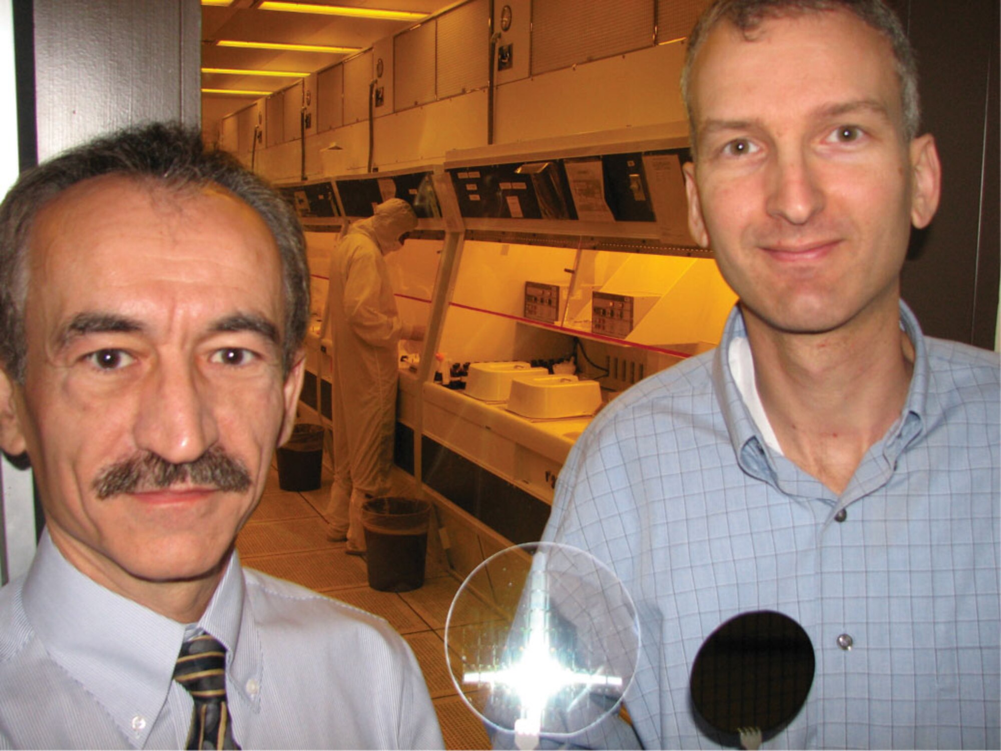 Air Force Research Laboratory's Dr. Burhan Bayraktaroglu and Dr. Kevin Leedy contrast transparent electronic circuits on quartz (left) to conventional circuits fabricated on silicon wafers (right) at the lab’s wafer fabrication facility.  (U.S. Air Force photo/Burhan Bayraktaroglu)