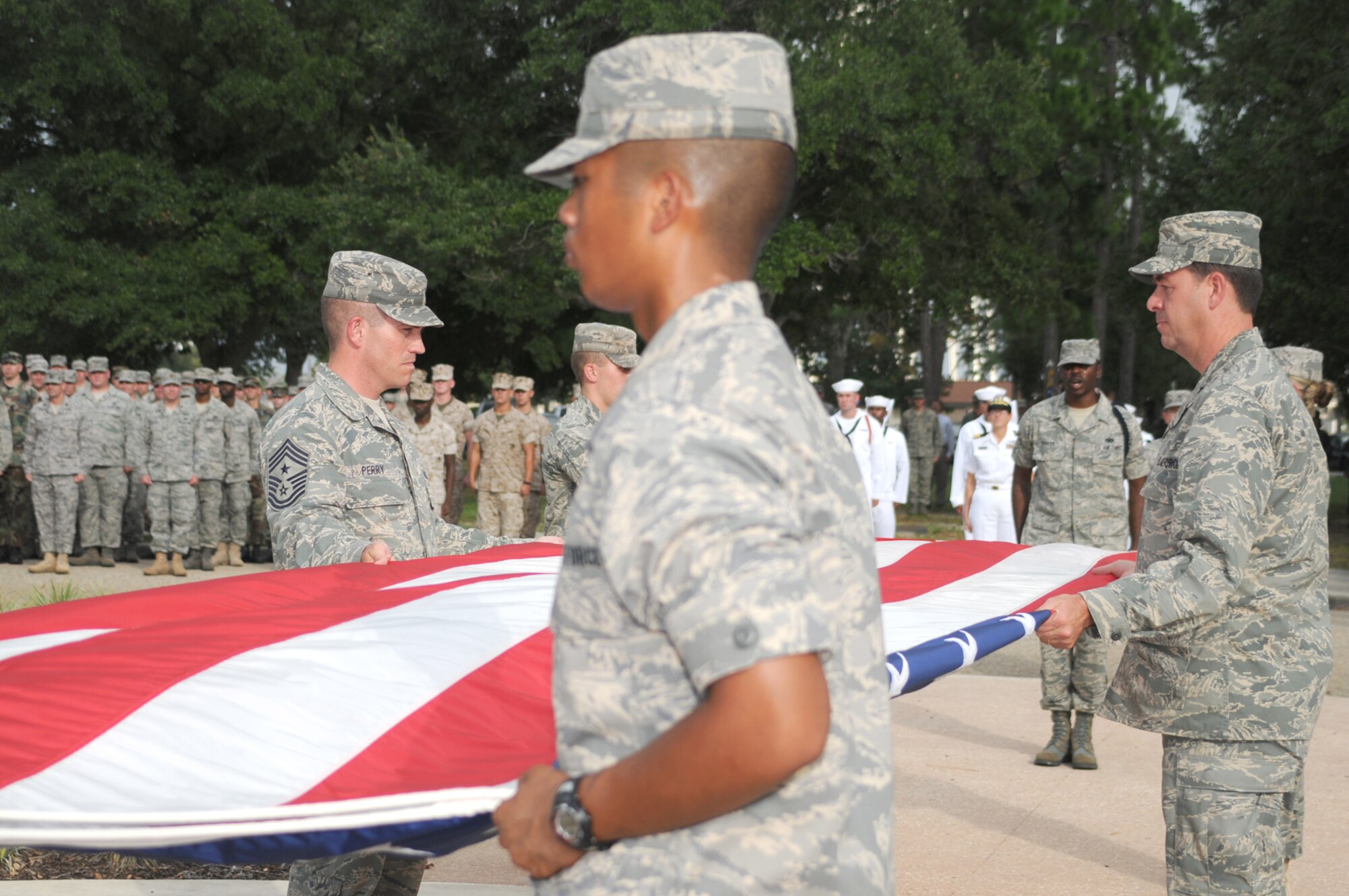 Left, Chief Master Sgt. Alex Perry, 81st Training Wing command chief; foreground, Airman Michaelangelo Cortez, 332nd Training Squadron; right, Brig. Gen. Greg Touhill, 81st TRW commander fold the flag in a retreat ceremony on Patriot Day at Keesler Air Force Base.  (U.S. Air Force photo by Kemberly Groue)
