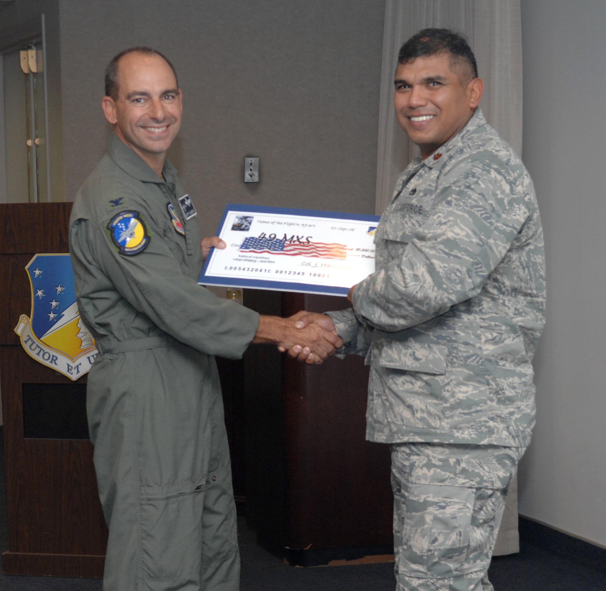Maj. Anthony Puente receives a check on behalf of the 49th Maintenance Squadron from Col. Jeff Harrigian, 49th Fighter Wing commander, at the 49 FW Headquarters building at Holloman Air Force Base, N.M., Sept. 10. The 49 MXS received a check for $1,500 to use for quality of life initiatives within the squadron for placing 2nd of the large squadrons in the Battle of Squadrons. (U.S. Air Force photo/Airman Sondra Escutia)