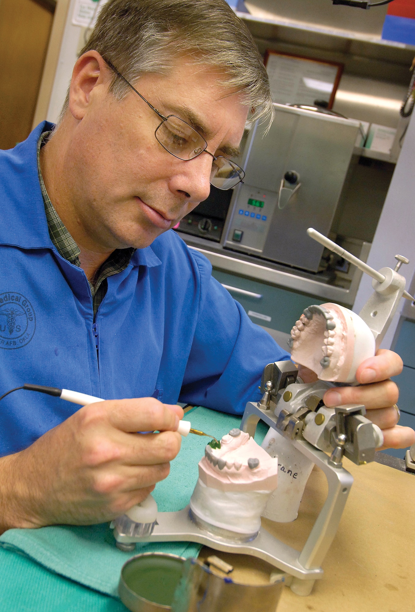 Technician Mark Cochrane copies fine indentions of a patient’s tooth surface into wax, one step in the intricate process of making crowns and other prosthetic restorations for military patients of the 72nd Dental Clinic. Eight Dental Clinic Lab technicians and a prosthodontist created over $724,000 in crowns, bridges, implants and mouth guards since last September.  Each appliance is hand made, from the initial teeth molds to wax molds, creating metal and ceramic appliances then matching shading and unique characteristics that add to realism. Mr. Cochrane compared the process to sculpting.  “When it’s done right, if you can’t even tell it’s artificial, you feel so good about it”, he said.  Technology new to the lab now gives quickly-deploying Airman necessary crowns in a fraction of the time.  Computer-Aided Design and Manufacturing equipment, or CAD/CAM, can create crowns for an Airman the same day when needed, versus traditional techniques that require up to 12 working days. (Air Force photo/Margo Wright) 

