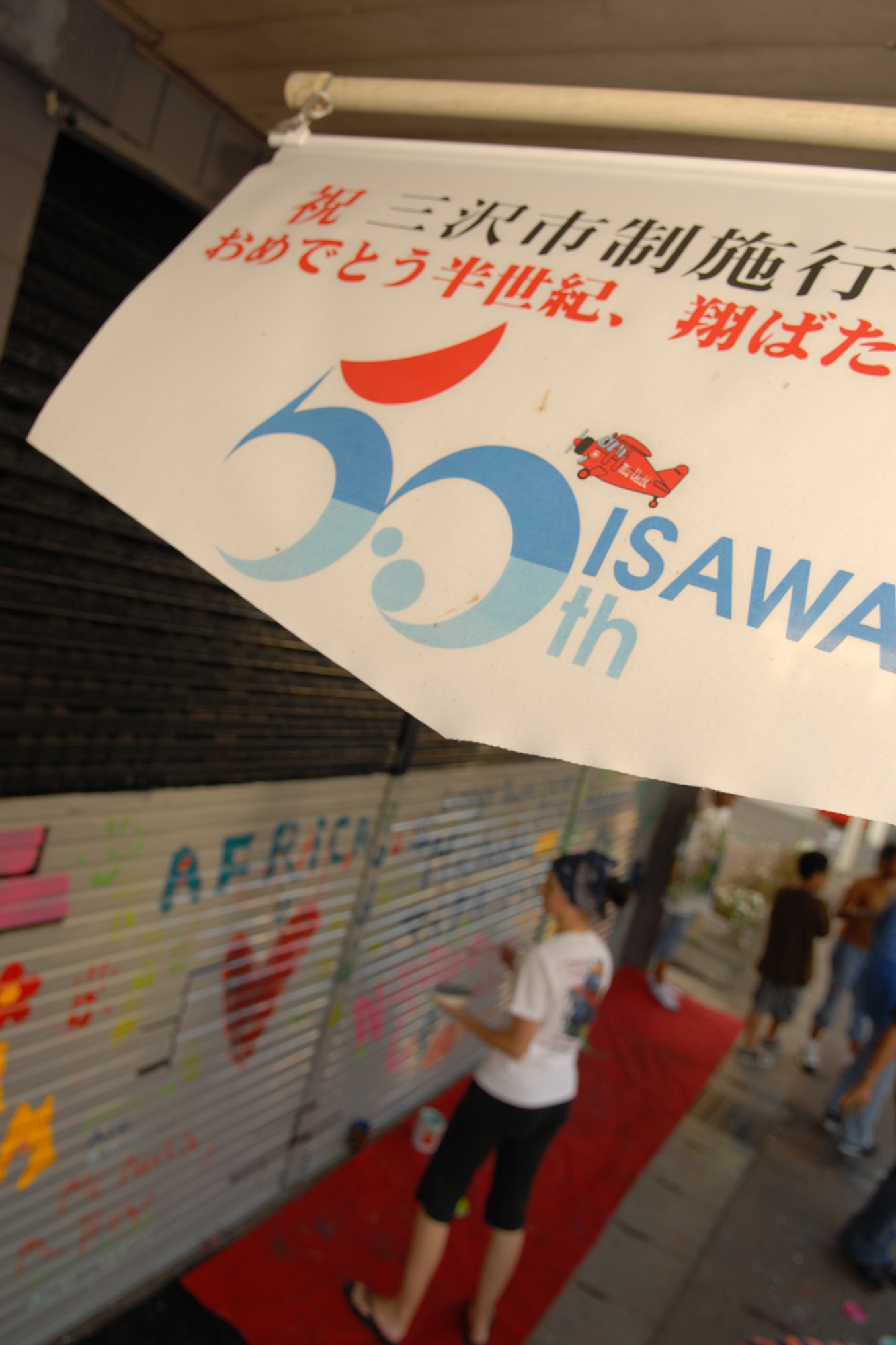MISAWA CITY, Japan -- As the Misawa 50th anniversary banner waves, children of the Lunney Youth Center wrap up the painting of a shutter Sept. 10, 2008. Five children from the Lunney Youth Center, along with their director and instructional coordinator, came out to help paint the shutter. The shutter was painted as part of a project to help beautify White Pole Road. (U.S. Air Force photo by Airman 1st Class Jamal D. Sutter)