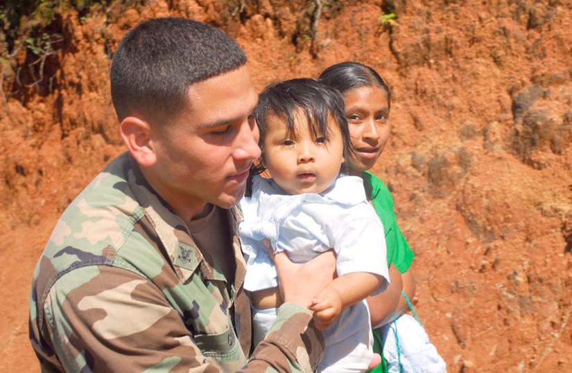SOTO CANO AIR BASE, Honduras - Navy Petty Officer 2nd Class Miguel Cruz, Joint Task Force-Bravo Security Forces, helps a mother carry a child up a hill in route to visit a helicopter for children's day Sept. 10 in Guajiquiro, Honduras. More than 400 children in two towns spent time with servicemembers from JTF-Bravo. (U.S. Air Force photo by Staff Sgt. Joel Mease)