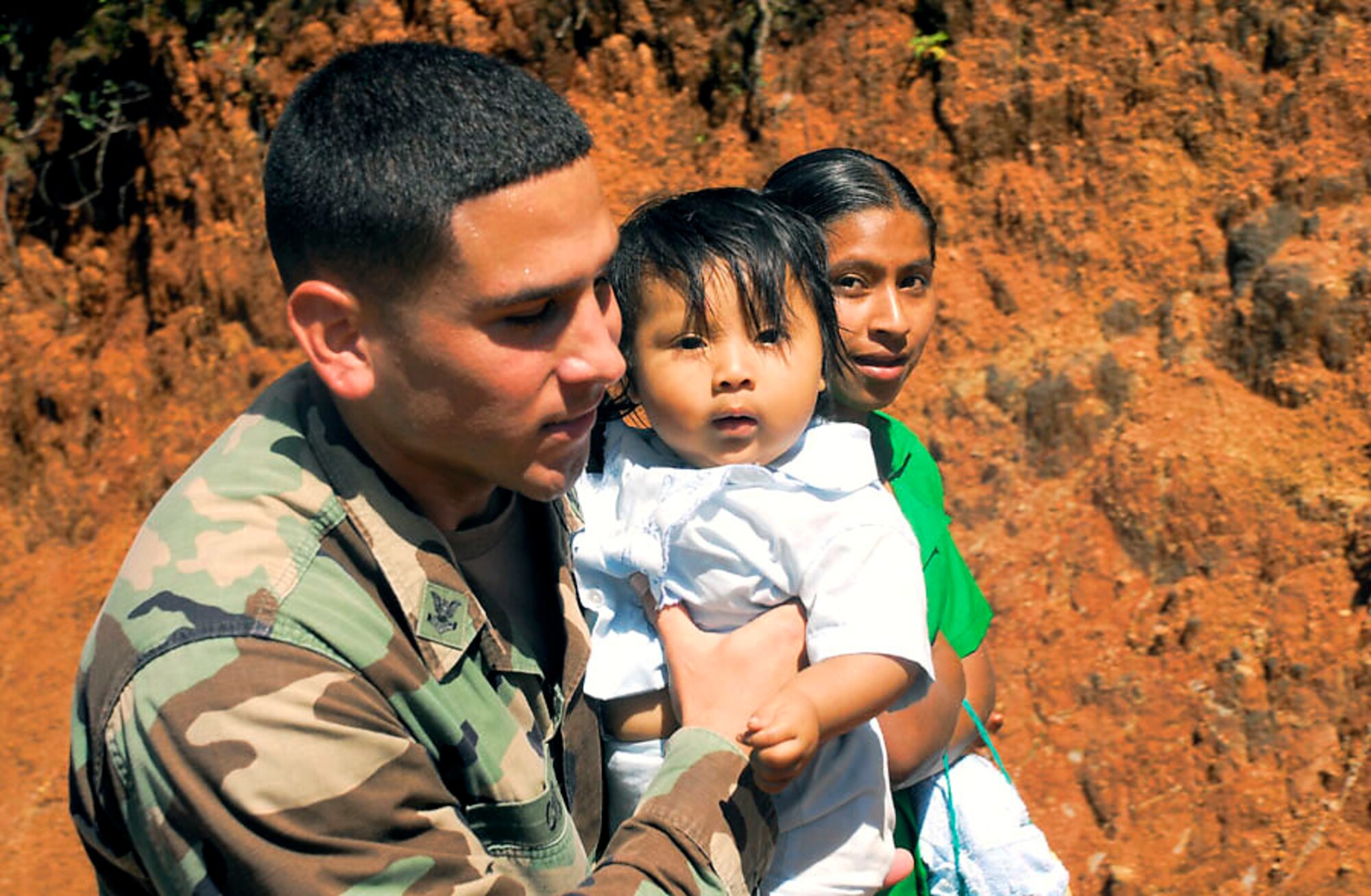 Navy Petty Officer 2nd Class Miguel Cruz helps a mother carry a child up a hill enroute to visit a helicopter for Children's Day Sept. 10 in Guajiquiro, Honduras. More than 400 children in two towns spent time with servicemembers from Joint Task Force-Bravo. Petty Officer Cruz is assigned to JTF-Bravo Security Forces. (U.S. Air Force photo/Staff Sgt. Joel Mease)
