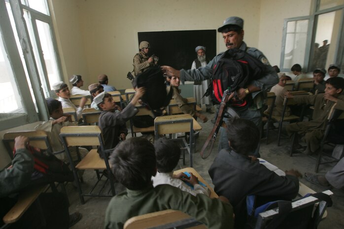 An Afghanistan National Policeman hands out backpacks to school children during the reopening of a boys’ school in Delaram, Afghanistan, Sept. 14. (U.S. Marine Corps photo by Sgt. Ray Lewis)