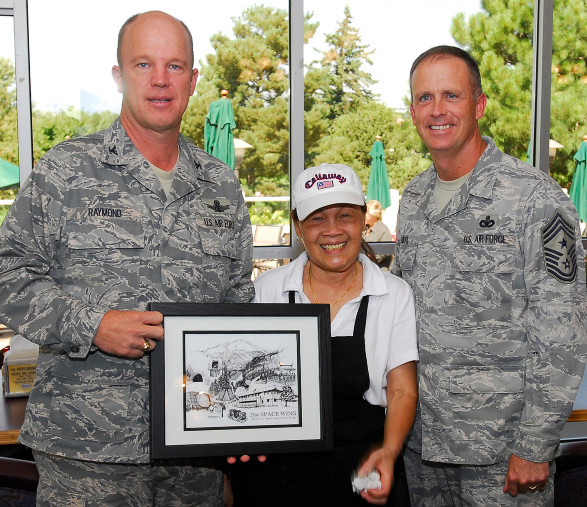 Tonie Gingrass (center) stands with Col. Jay Raymond, 21st Space Wing commander (left) and Chief Master Sgt. Timothy Omdal, 21st SW command chief Aug. 27 as she receives the wing’s longevity award for 20 years of service. The award, presented at Peterson Air Force Base’s Silver Spruce Golf Course, culminates Mrs. Gingrass’s career at the golf course where she is retiring soon and her recent acceptance in becoming a U.S. citizen after moving the U.S. 32 years ago. Colonel Raymond also pointed out during the ceremony he originally met Mrs. Gingrass several years ago when he was a captain. (U.S. Air Force photo/Robb Lingley)