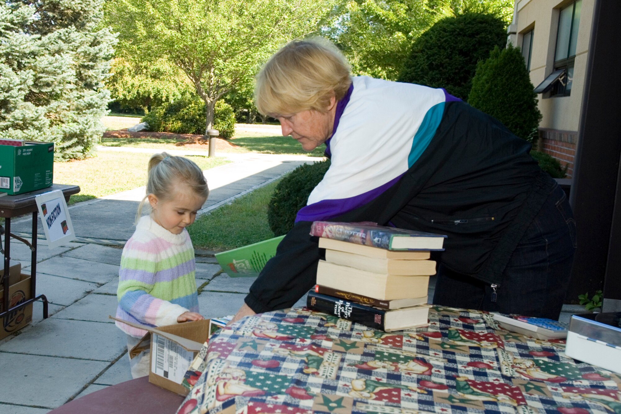 HANSCOM AFB, Mass. -- Jane Doherty, Hanscom library aide, shows Amber Blake a box of children's books during a used book sale held outside the Hanscom Library Sept. 11. Library patrons can not only look through the library's many books, but also browse through magazines and listen to CDs and watch movies in the Library's audiovisual room. (U.S. Air Force photo by Rick Berry)