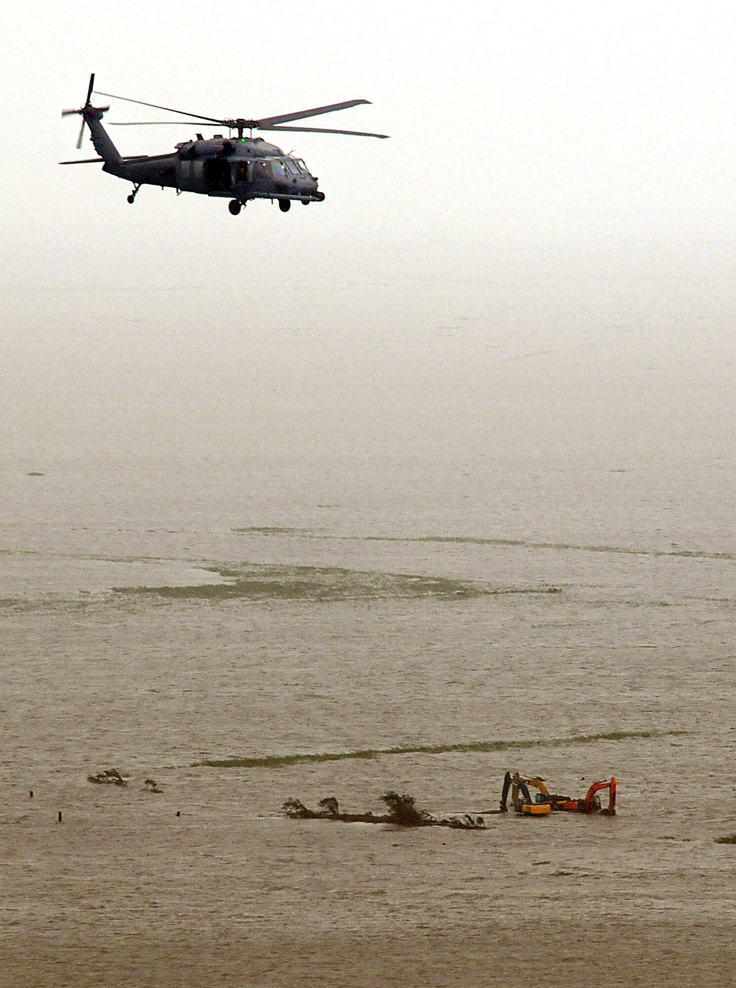 An HH-60G Pave Hawk helicopter assigned to the 331st Air Expeditionary Group passes over three massive hydraulic excavators sitting in flood waters from Hurricane Ike.  Deployed from the 920th Rescue Wing at Patrick Air Force Base, Fla., the pararescuemen, along with aircrews, two HH-60G Pave Hawk helicopters and two HC-130P/N refueling aircraft, rescued 17 people from the small Texas town of Nederland Sept. 13. (U.S. Air Force photo/Tech. Sgt. Paul Flipse)