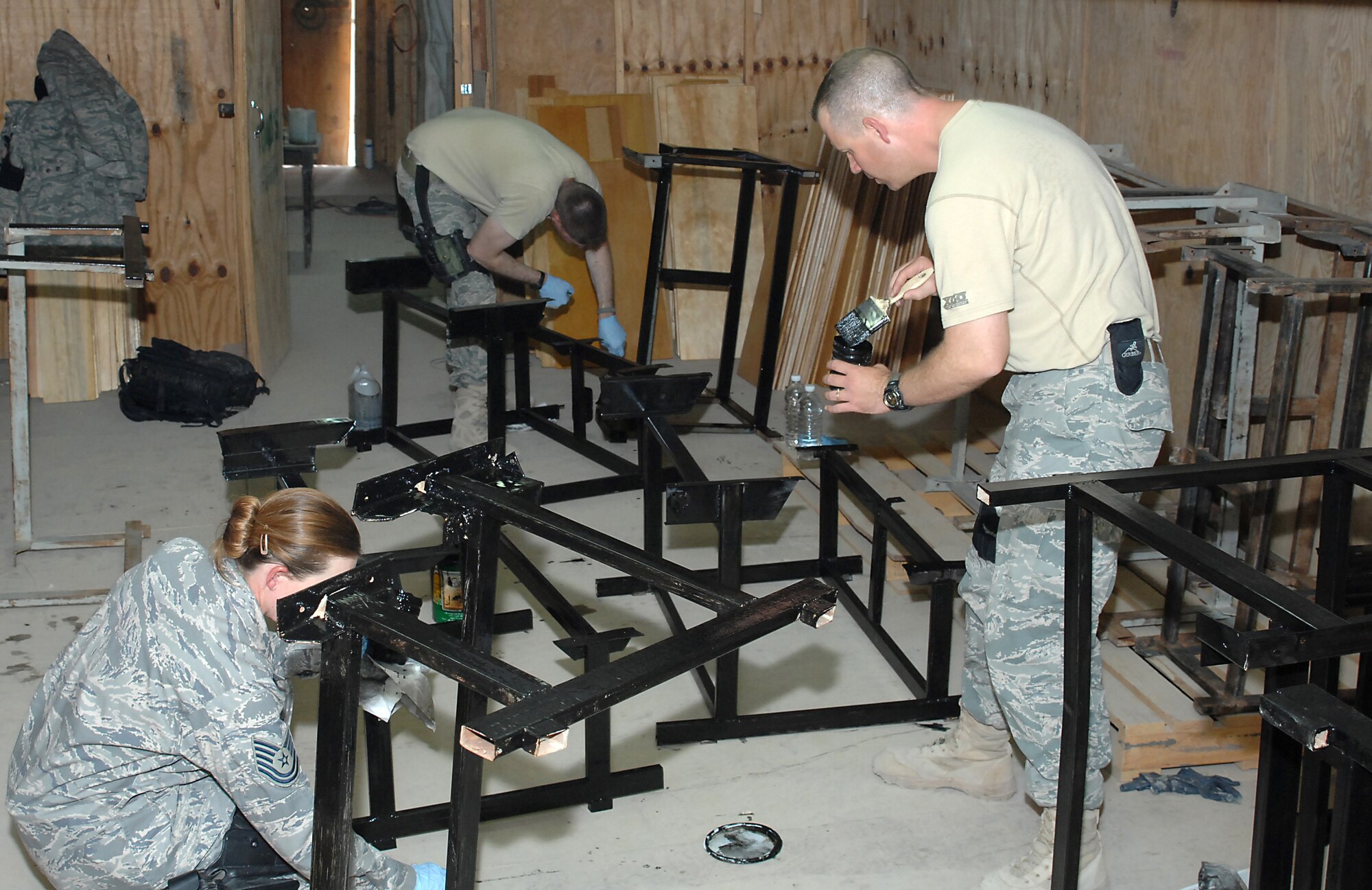 ALI BASE, Iraq -- Airmen assigned to the 407th Provost Marshal Office paint lacquer on steel desk frames Sept. 13, 2008. They and others here volunteered to refurbish 150 desks that, once finished, 450 students from two Muthanna Province elementary schools will receive "new" desks. (U.S. Air Force photo/Tech. Sgt. Francesca Popp)