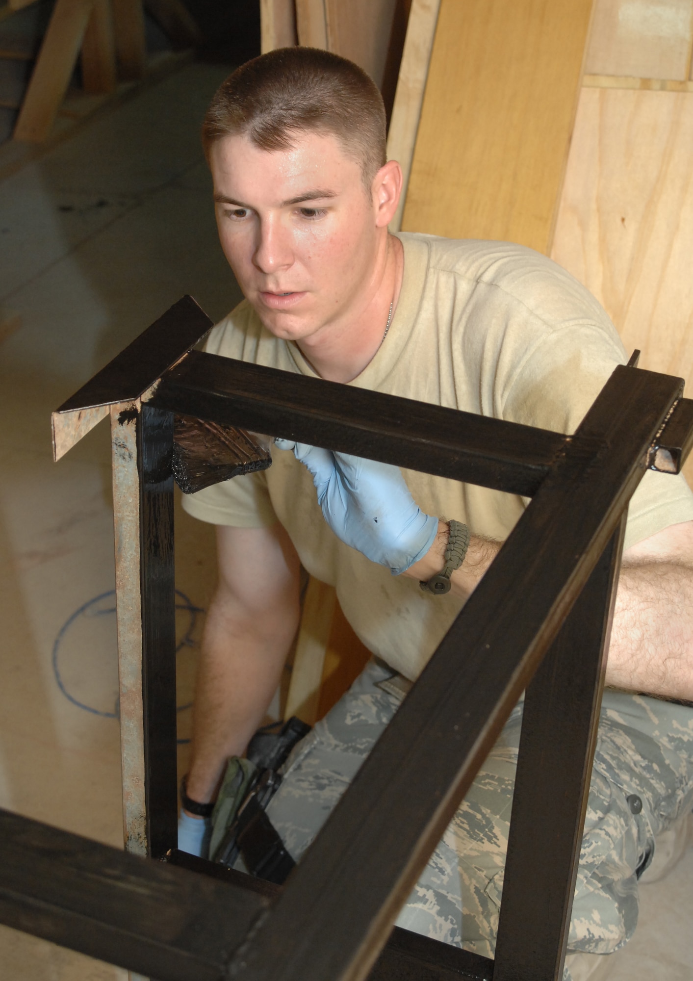 ALI BASE, Iraq -- Staff Sgt. Charles Coles, 407th Provost Marshal Office traffic accident investgator, applies black lacquer to a steel desk frame Sept. 13, 2008. He and others here volunteered to refurbish 150 desks that, once finished, 450 students from two Muthanna Province elementary schools will receive "new" desks. Coles, who hails from Surprize, Ariz., is deployed from Eglin Air Force Base, Fla. (U.S. Air Force photo/Tech. Sgt. Francesca Popp)
