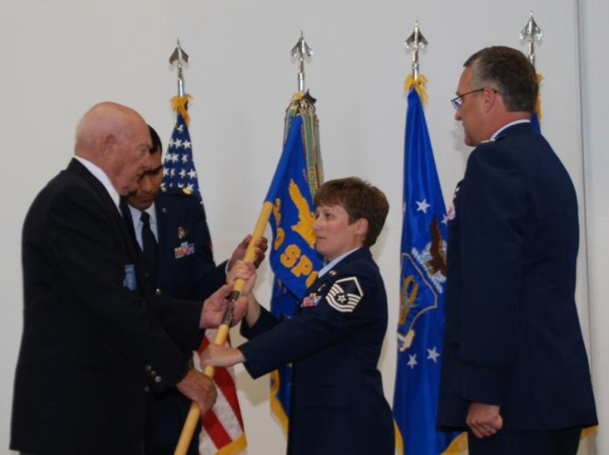 COLORADO SPRINGS, Colo. -- Master Sgt. Melanie Sekerak passes the 380th Space Control Squadron, formerly the 380th Bombardment Squadron, guidon to retired Col. Bill Bower, former commander of the 310th Bomb Group during World War II,  during the 380th SPCS reactivation ceremony. Col. Jeffrey Ansted, 310th Space Wing commander, waits to receive the guidon. (courtesy photo)