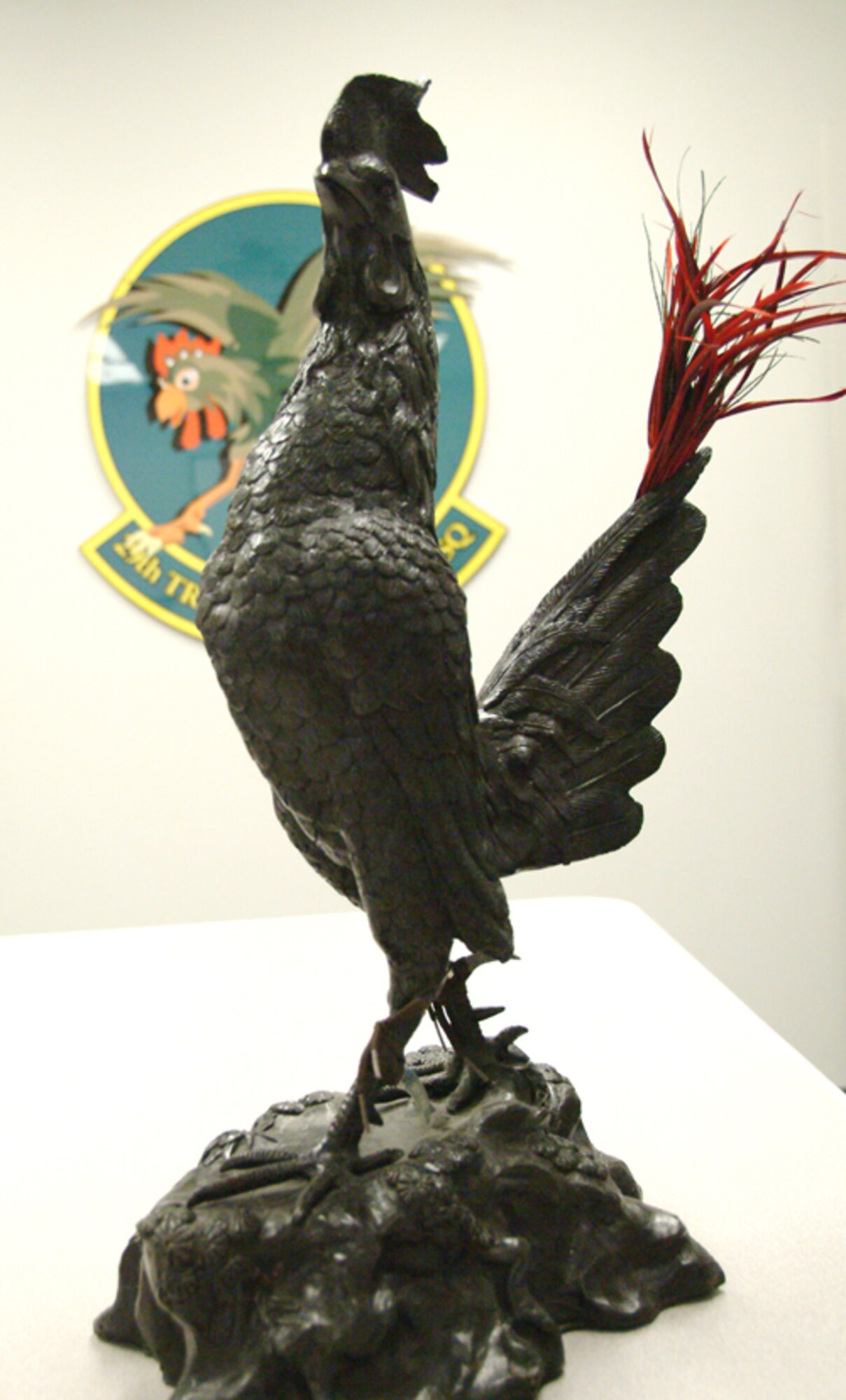 A statue of the 29th Test Systems Squadron mascot the "Fighting Gamecock" sits in front the squadron's patch located in the squadron's office.  The Gamecock has represented the squadron since 1935.  The squadron celebrates its 90th birthday Oct 10 with an open house and cook-out.  Photo by Staff Sgt. Samuel King Jr.