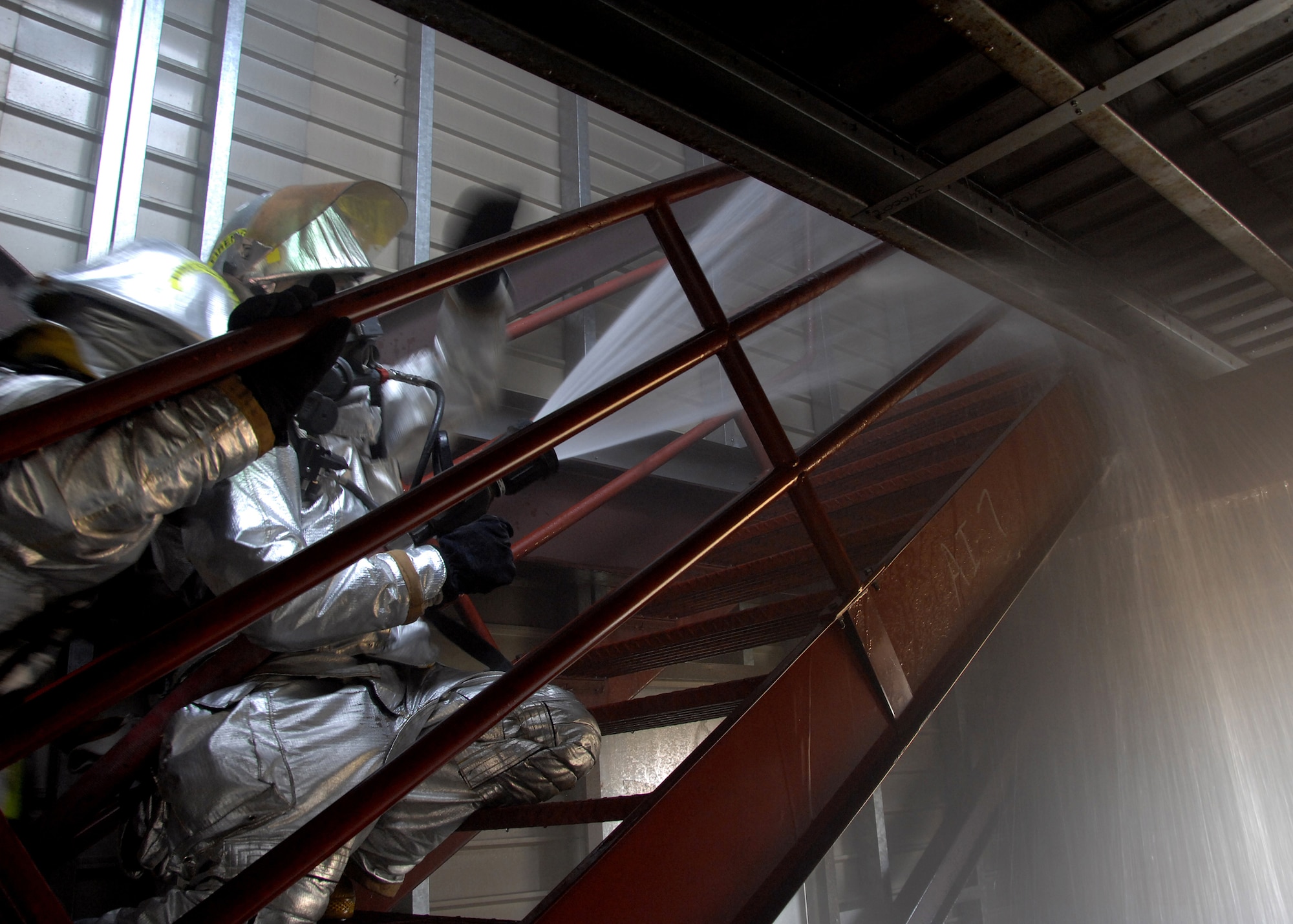 Two firefighters from the 354th Civil Engineer Squadron fire protection flight, advance up a stairwell a toward a floor on fire during a training operation on Sept. 13, 2008, at the live fire training area on Eielson AFB, Alaska. The Firefighters focus the jets of water toward beacons with red flashing lights, designed to emulate a fire. (U.S. Air Force photo by Airman 1st Class Willard E. Grande II)