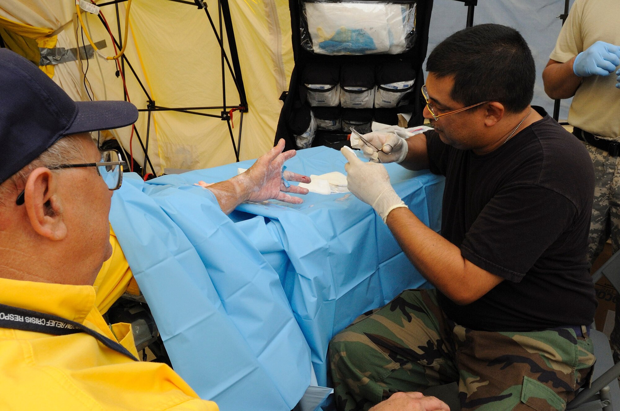 Air Force Captain Fabio Delarosa, a physician's assistant from Task Force Ike, Texas Military Forces prepares to stitch up an emergency responder who gashed his finger while setting up emergency equipment at Ball High School, Galveston, Texas. September 17, 2008 ( Air Force Photo by: SMSgt Elizabeth Gilbert) CLEARED