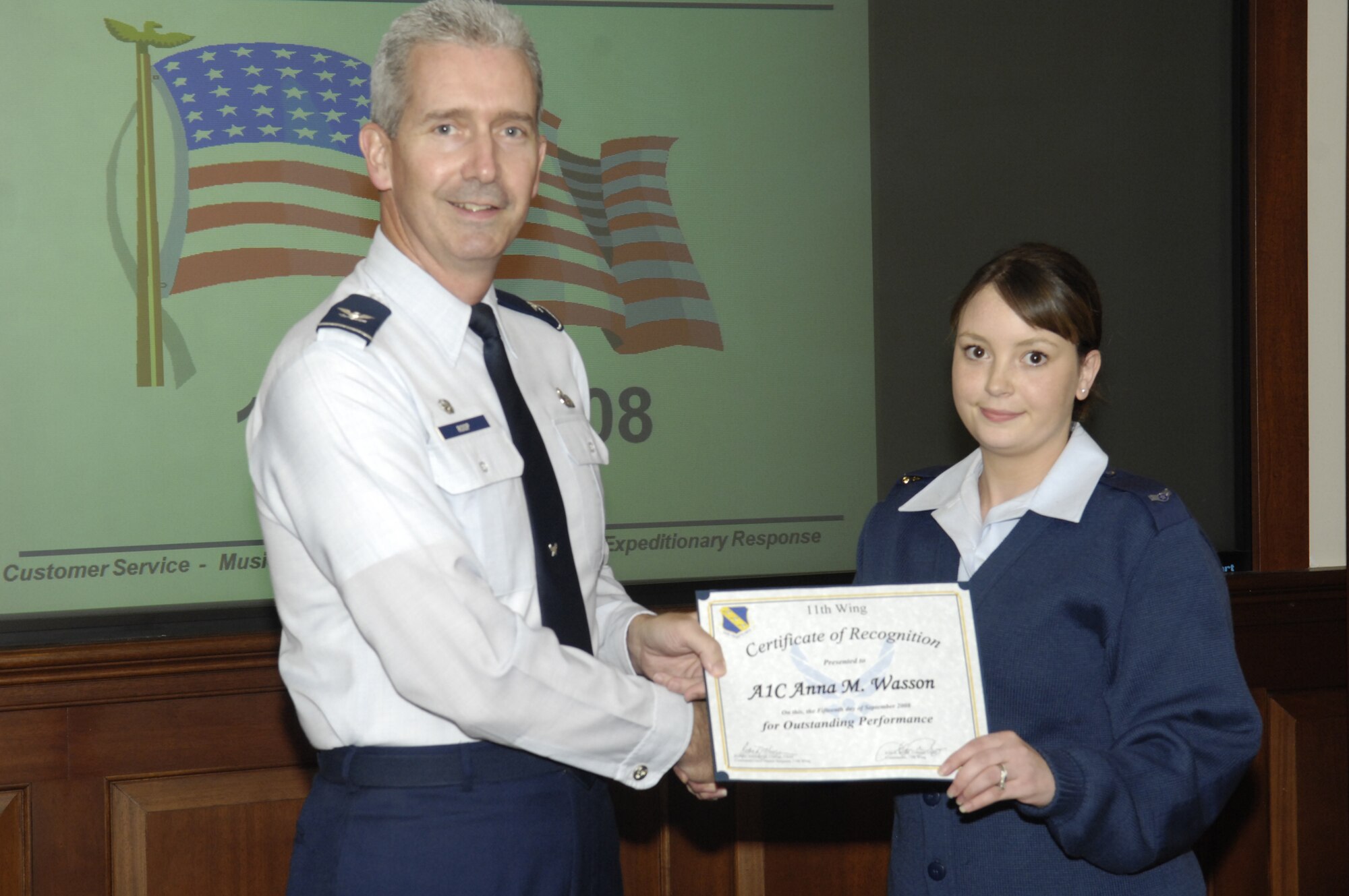 Col. Jon A. Roop, 11th Wing commander, presents a certificate and coin to Airman 1st Class Anna M. Wasson, 11th Operations Group, Sept. 15 in the wing conference room. Airman Wasson was recognized for spearheading the validation of 450 network accounts and being named the 11th Wing Information Manager of the Quarter.  (U.S. Air Force photo by Senior Airman R. Michael Longoria)