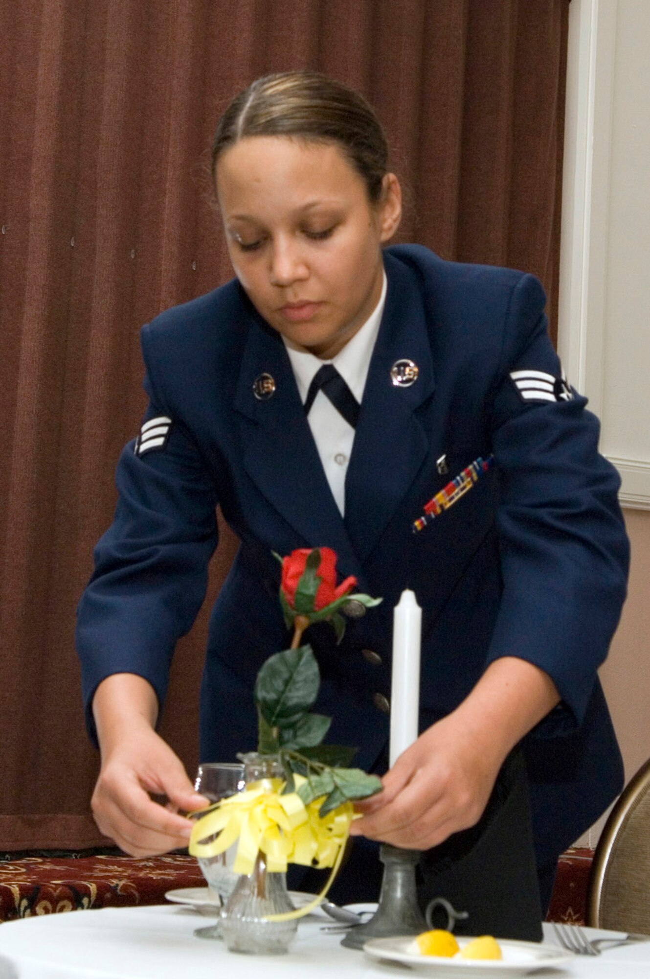 The yellow ribbon on the vase represents the yellow ribbons worn on the lapels of the thousands who demand with unyielding determination a proper accounting of our comrades who are not among us tonight.

Senior Airman Amanda Carter, 66th Medical Operations Squadron dental technician at Hanscom Air Force Base, Mass., leads a ceremony honoring prisoners of war and servicemembers missing in action. Such ceremonies are held before many official base events to honor and remember fallen comrades. National POW/MIA Day is Sept. 19. (U.S. Air Force photo/Mark Wyatt)