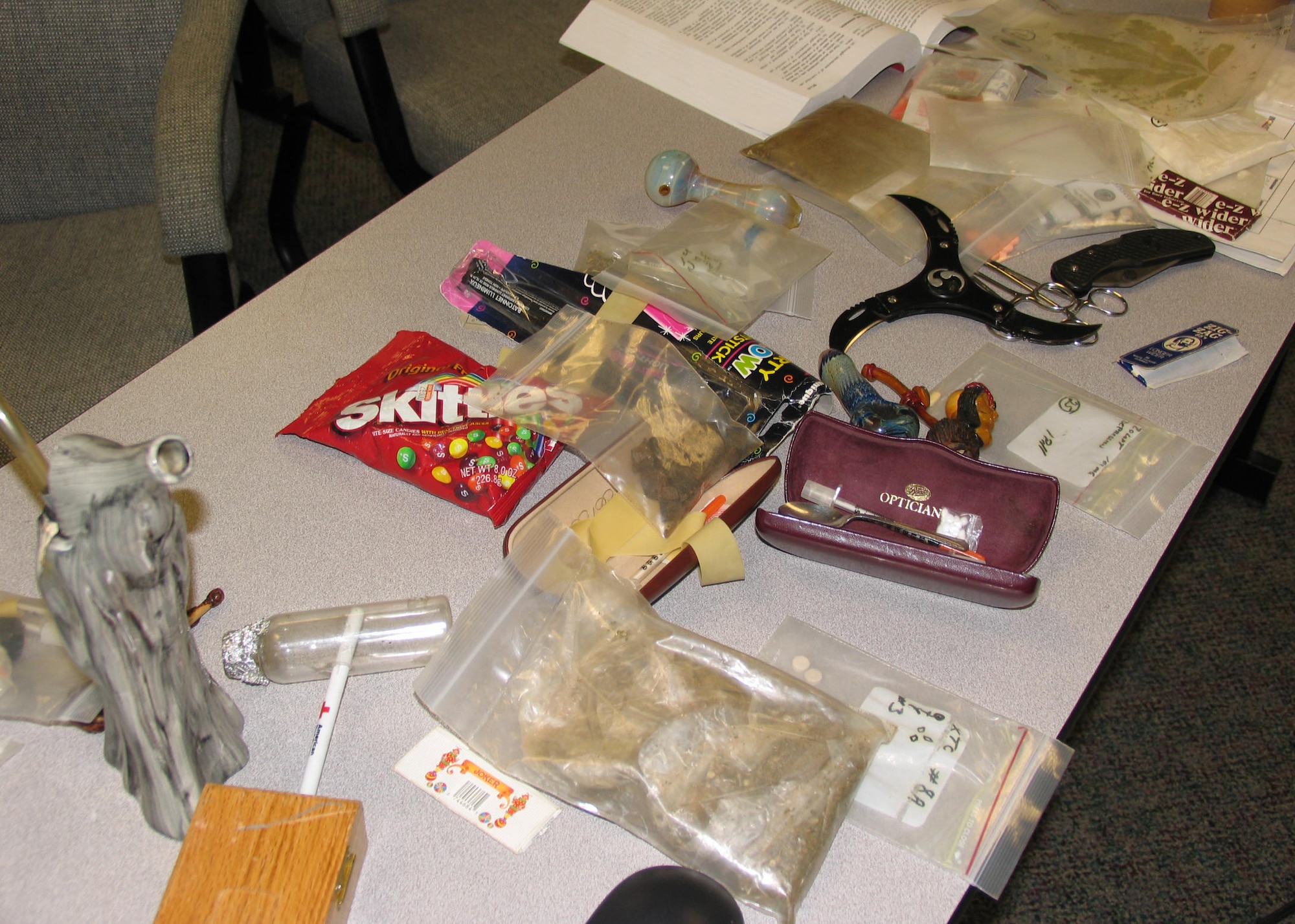 HANSCOM AFB, Mass. -- A table displays pipes, baggies of cocaine, heroin and marijuana, needles, and various knives for 66th Security Forces Squadron Airmen attending a drug familiarization training session Sept. 17. All of the table's contents were confiscated by Saugus, Mass., police officers during drug arrests. The course was taught by a narcotics detective from the Saugus Police Department. (U.S. Air Force photo by 1st Lt. Lisa Spilinek)