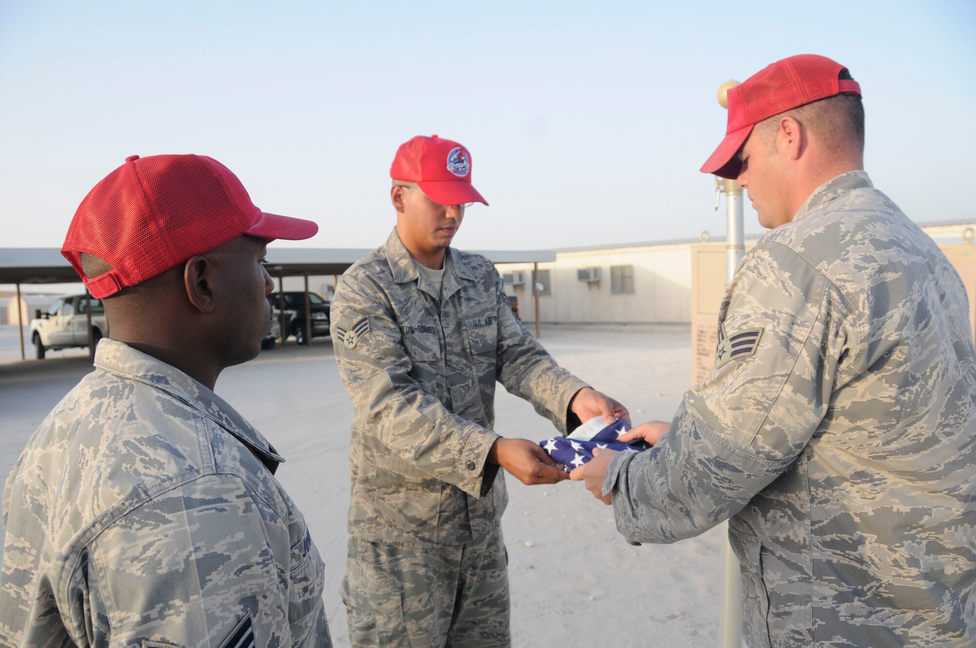 Staff Sgt. LaCourtney Jones waits to call commands while Senior Airman Antonio Santos-Torres and Senior Airman Jason Freytag fold the U.S. flag during retreat Sept. 19, 2008, at an undisclosed air base in Southwest Asia. Airman Santos-Torres is a native of Ponce, Puerto Rico. Airman Freytag is a native of Temple, Texas and Sergeant Jones is a native of Augusta, Ga. All three are supply personnel assigned to the 1st Expeditionary RED HORSE Group deployed in support of Operations Iraqi Freedom, Enduring Freedom and Joint Task Force-Horn of Africa from Hurlburt Field, Fla.  Everyday the RED HORSE Group raises and lowers the flag in front of their compound for reveille and retreat. (U.S. Air Force photo by Staff Sgt. Darnell T. Cannady/Released)