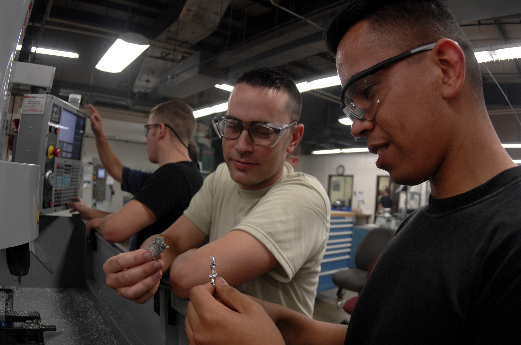 MOODY AIR FORCE BASE, Ga. -- Senior Airman Juan Ruiz (right) and Airman Michael McClellan, 23rd Equipment Maintenance Squadron aircraft metals technology, examine small scraps of aluminum fused together by the heat of a mill cutting tool here August 27.  The two airmen discuss how the temperature of the cutting tool fused the small pieces of metal together. (U.S. Air Force photo by Senior Airman Javier Cruz) 