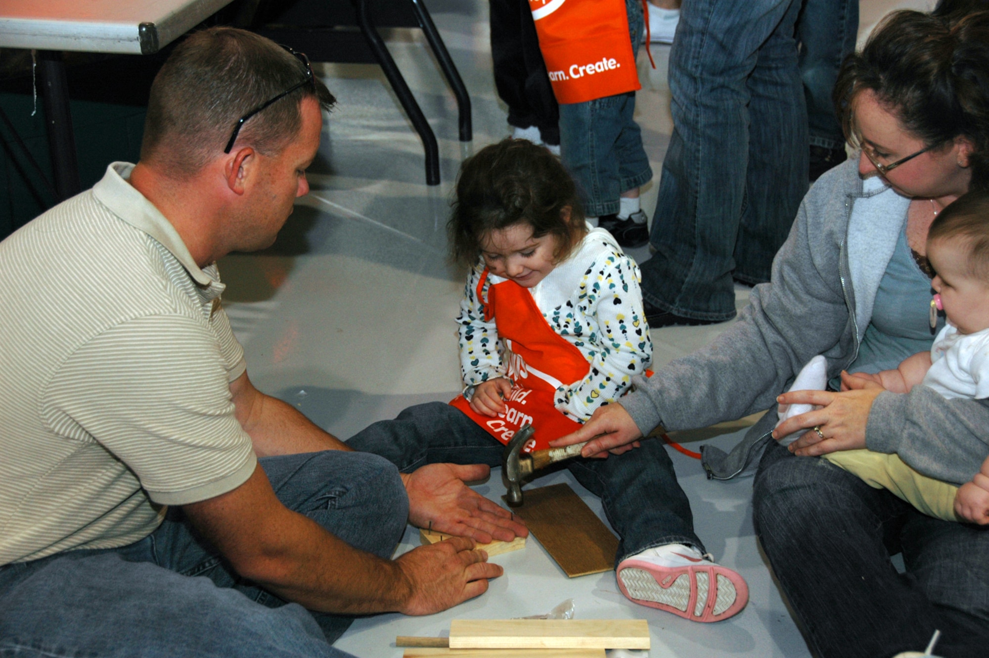 With 8-month old Shelby in one hand, Kari Cropper uses her other hand to hammer a nail for her 3-year-old daughter, Kelsey, during the 931st Air Refueling Group's 2008 Family Day Picnic. Trusting Kari's aim is her husband, Tech. Sgt. Edward Cropper from the 931st Aircraft Maintenance Squadron. Building materials for children's projects at the picnic were donated by Home Depot.  The company's donation has become a tradition at 931st picnics. (U.S. Air Force photo/Senior Airman Connor Burkhard)