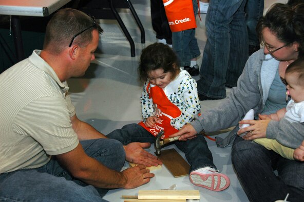 With 8-month old Shelby in one hand, Kari Cropper uses her other hand to hammer a nail for her 3-year-old daughter, Kelsey, during the 931st Air Refueling Group's 2008 Family Day Picnic. Trusting Kari's aim is her husband, Tech. Sgt. Edward Cropper from the 931st Aircraft Maintenance Squadron. Building materials for children's projects at the picnic were donated by Home Depot.  The company's donation has become a tradition at 931st picnics. (U.S. Air Force photo/Senior Airman Connor Burkhard)