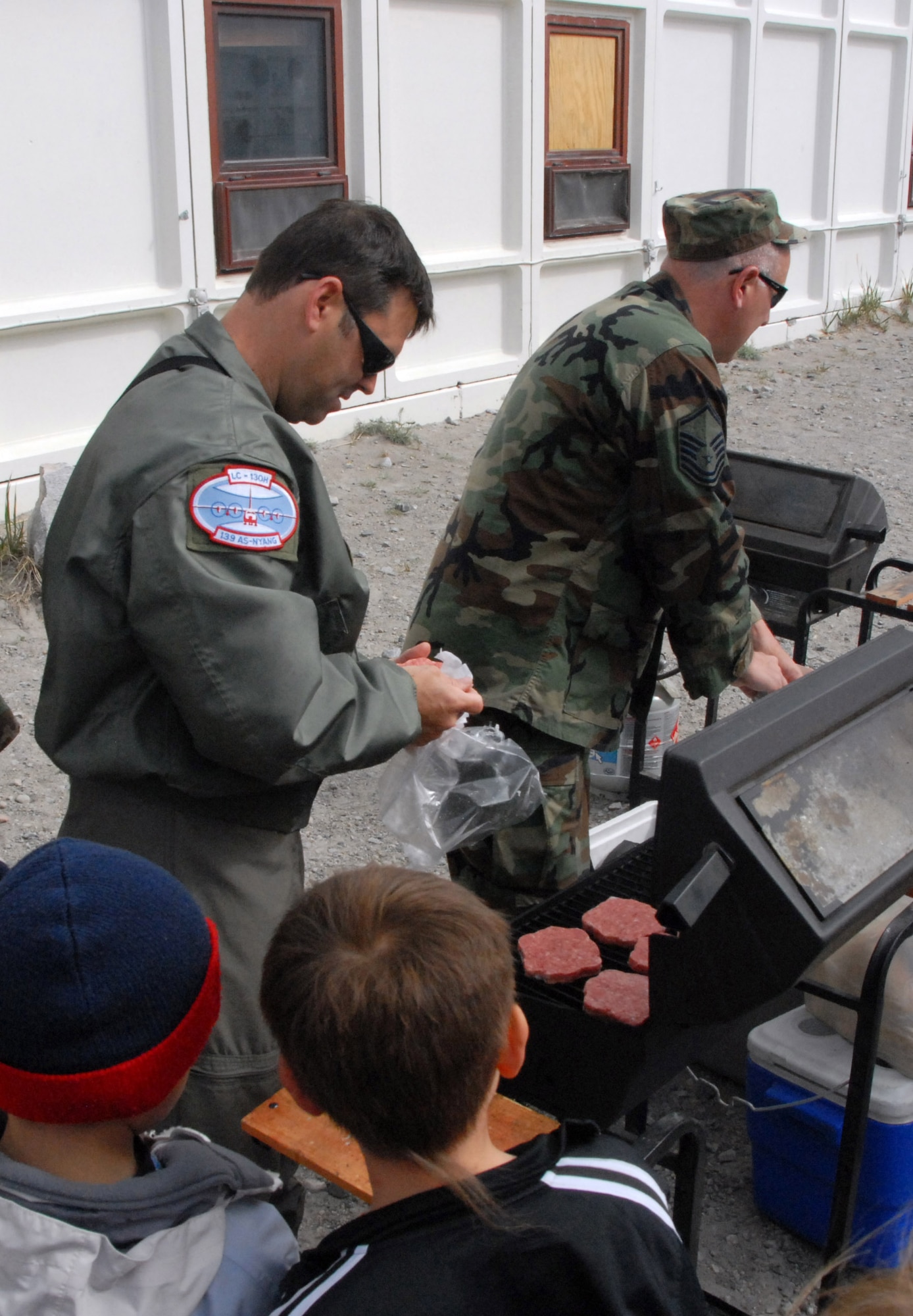 Kids wait patiently as Tech. Sgt. Michael Spiak (left) and Master Sgt. Pete Latniak grill some hamburgers during a community day 109th Airlift Wing members organized for the Greenland school. (U.S. Air Force photo by Master Sgt. Christine Wood)