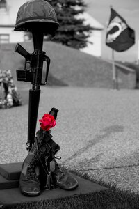 ELMENDORF AIR FORCE BASE, Alaska -- A Fallen Warrior Memorial stands upright as the POW/MIA flag waves in the background during the POW/MIA ceremony Sept. 19. The Fallen Warrior Memorial consists of items that represent different aspects of the battle field. The rifle represents the warriors weapon, the helmet represents the armor, the boots and nametags represents the fallen warrior itself, and the single rose represents the countries love, honor and mourning for the fallen warrior. (U.S. Air Force photo illustration/Staff Sgt. Joshua Garcia)