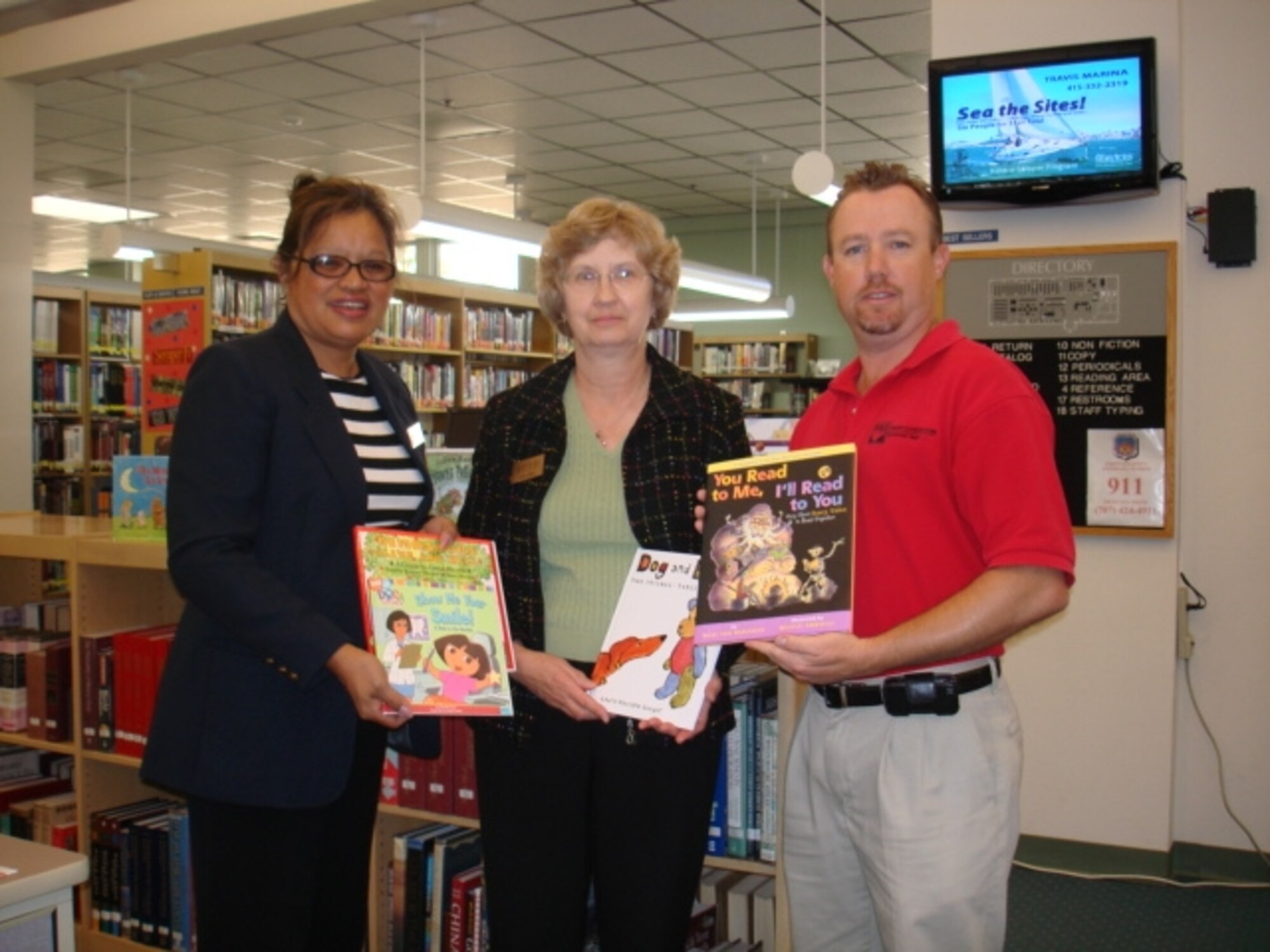 Annette Corsey, (left), DeCA Travis store administrator, Marie Ludwig, library director and Andrew Davies, military resale director receive a book donation Sept. 18 at the Mitchell Memorial Library. Travis was one of four out of 200 worldwide military installations selected for a donation of 120 children's books valued at approximately $1,000 from a large corporate company. The donation is part of the Reading is Fundamental program for that company. (U.S. Air Force photo)