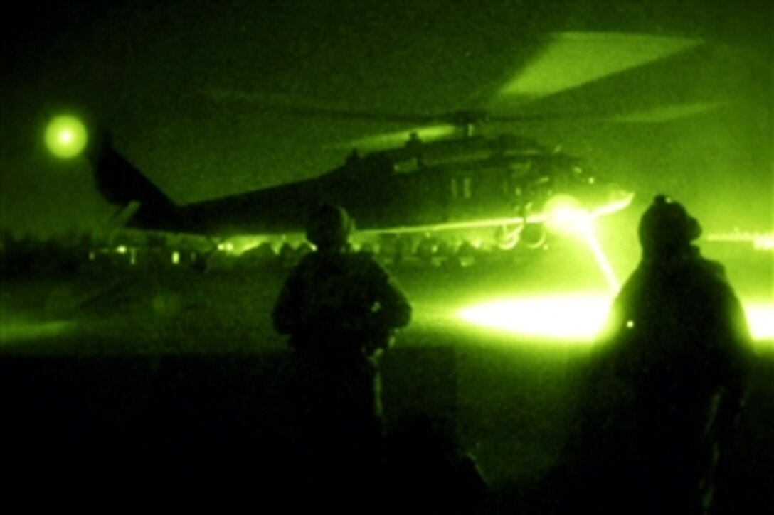 Seen through a night-vision device, U.S. Army Sgt. Alex Plitsas, left, and Spc. John Rosa, wait for a UH-60 Black Hawk helicopter to land on Forward Operating Base Liberty, Iraq, Sept. 20, 2008. The soldiers, both assiged to the 4th Infantry Division's 312th Psychological Operation Company, were preparing to take part in a leaflet drop mission.